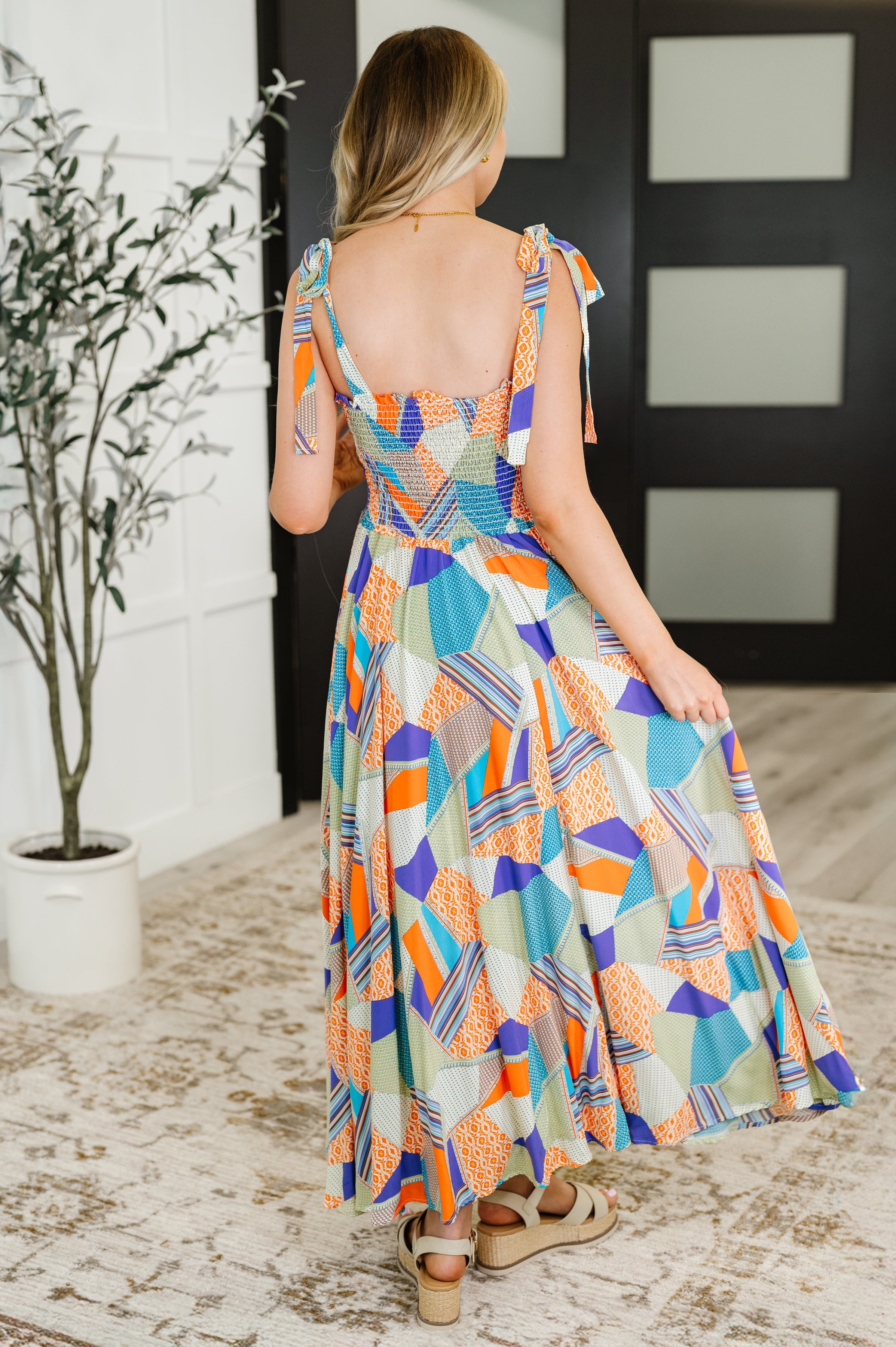 Woman wearing a colorful geometric patchwork dress with tie shoulder straps and smocked back detail indoors
