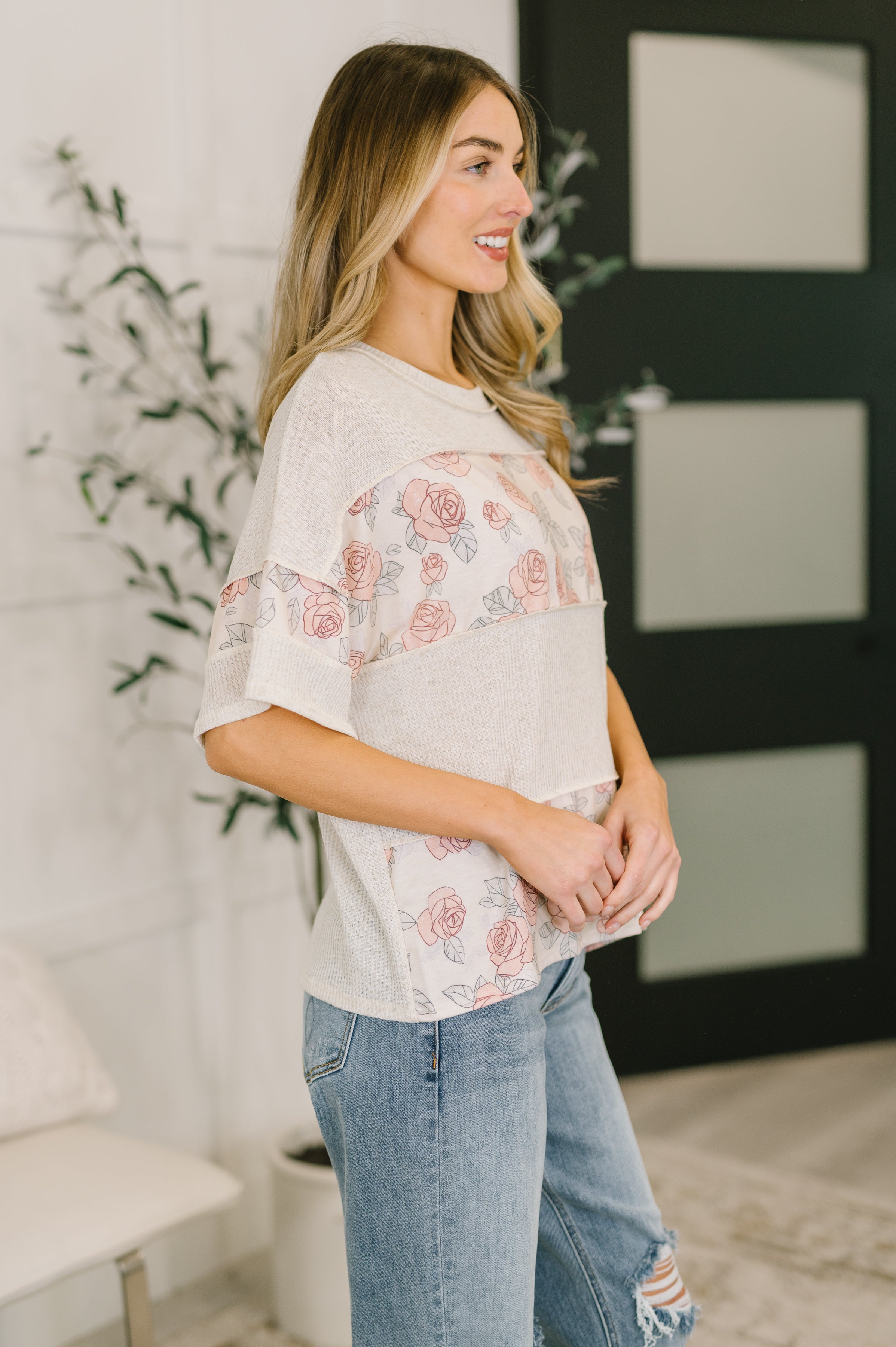 Woman wearing relaxed pink color block top with floral panels paired with ripped light blue jeans indoors