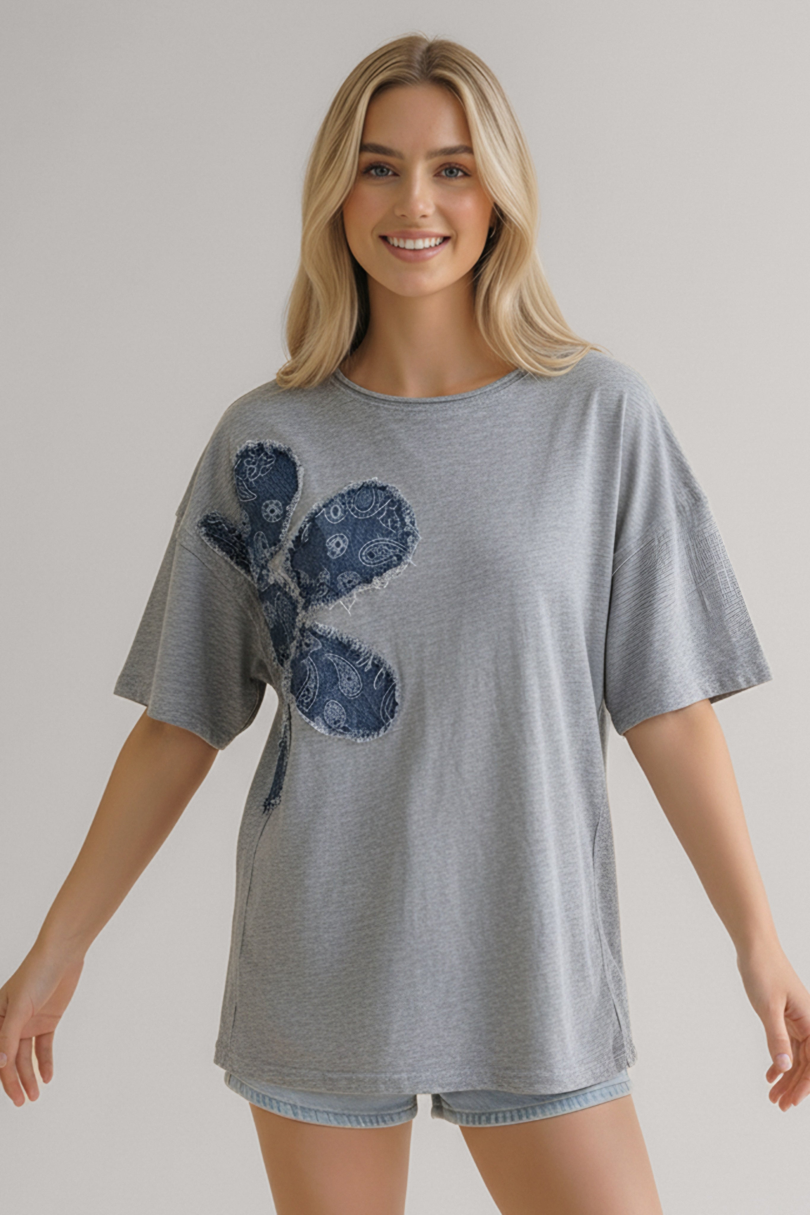 Woman wearing a heather grey top with oversized short sleeves and a large navy floral appliqué on the front