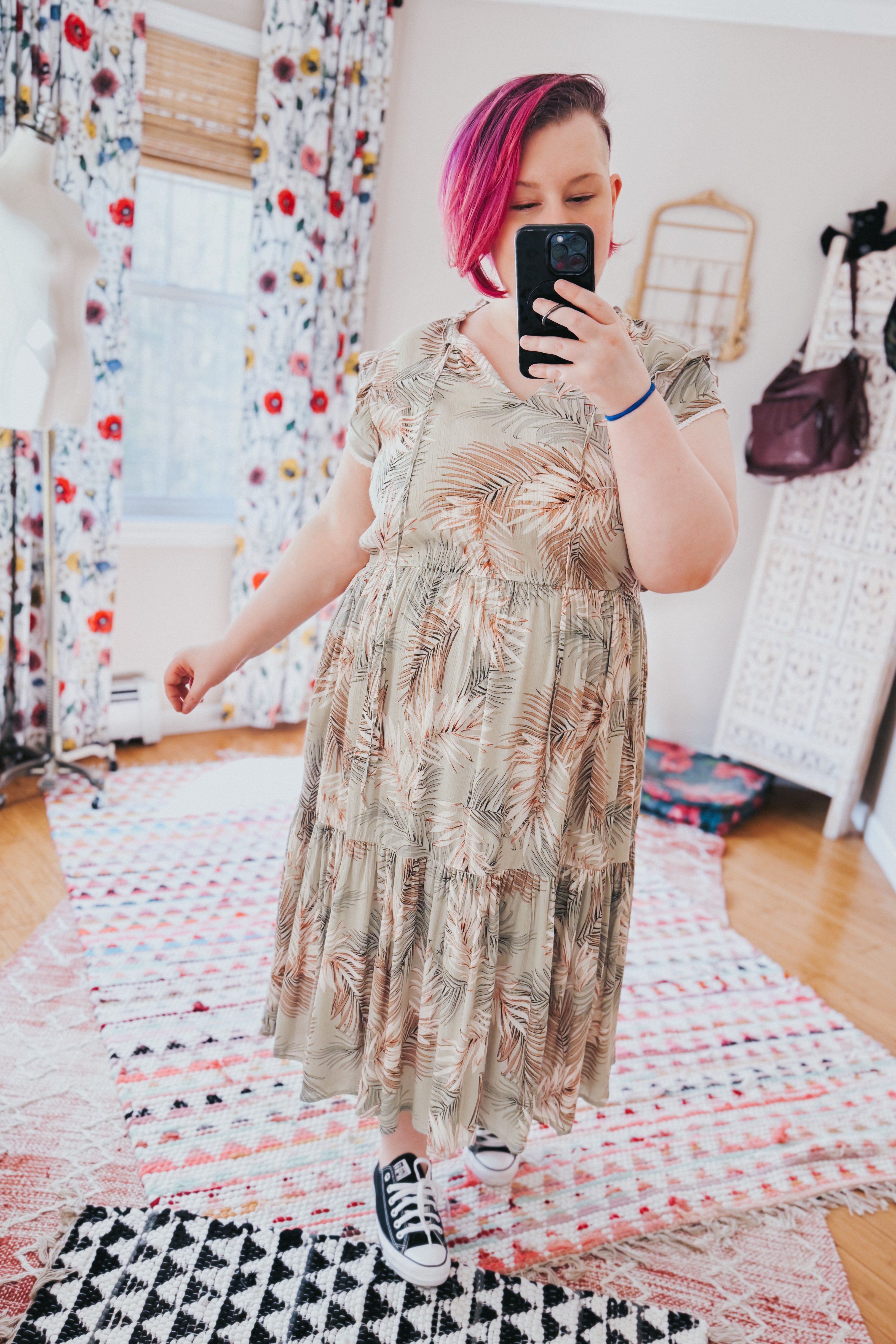 Woman with short pink hair wearing a tiered midi dress with palm leaf print and black sneakers indoors