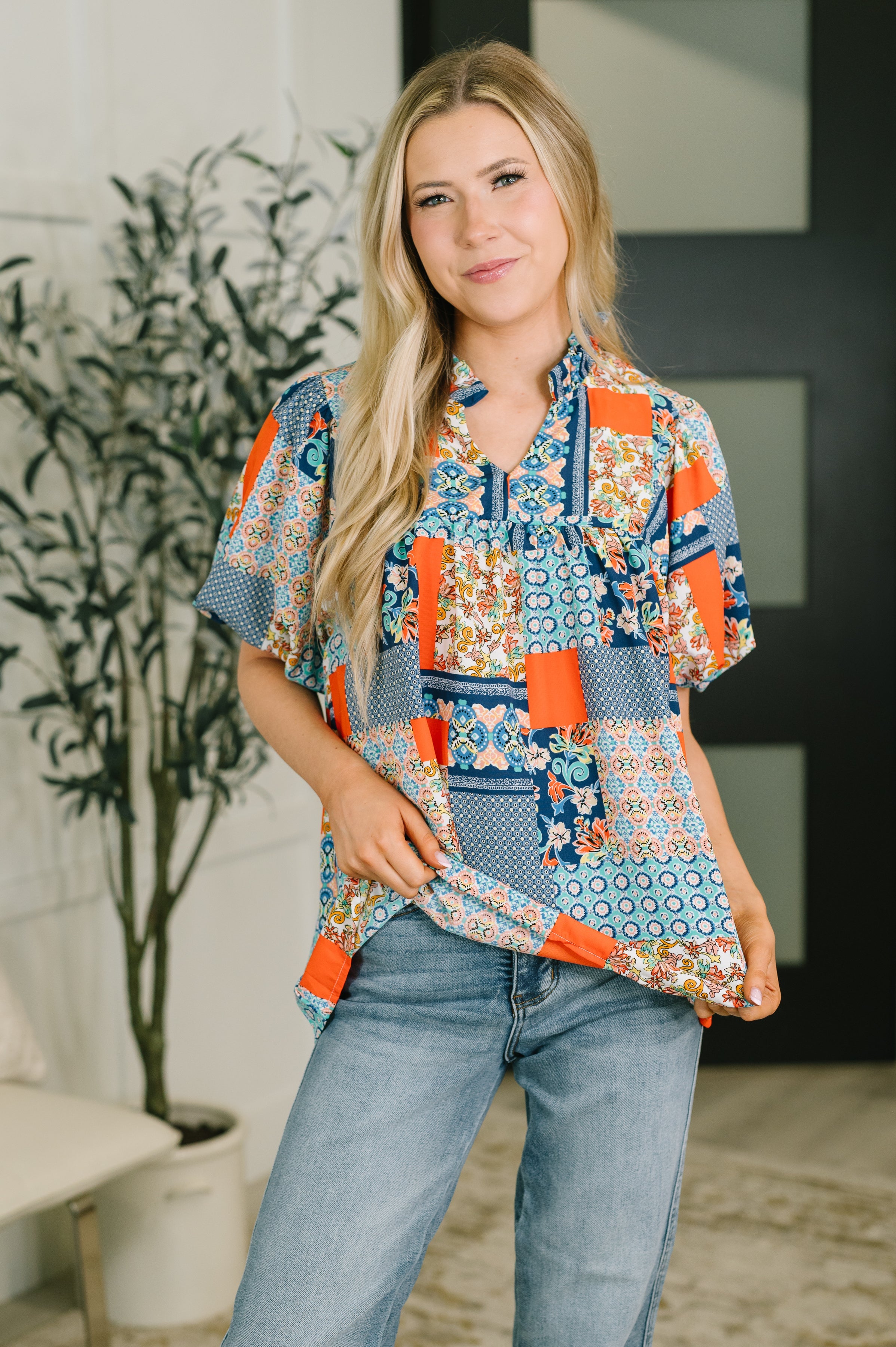Woman wearing a blue patchwork blouse with puff sleeves and jeans indoors