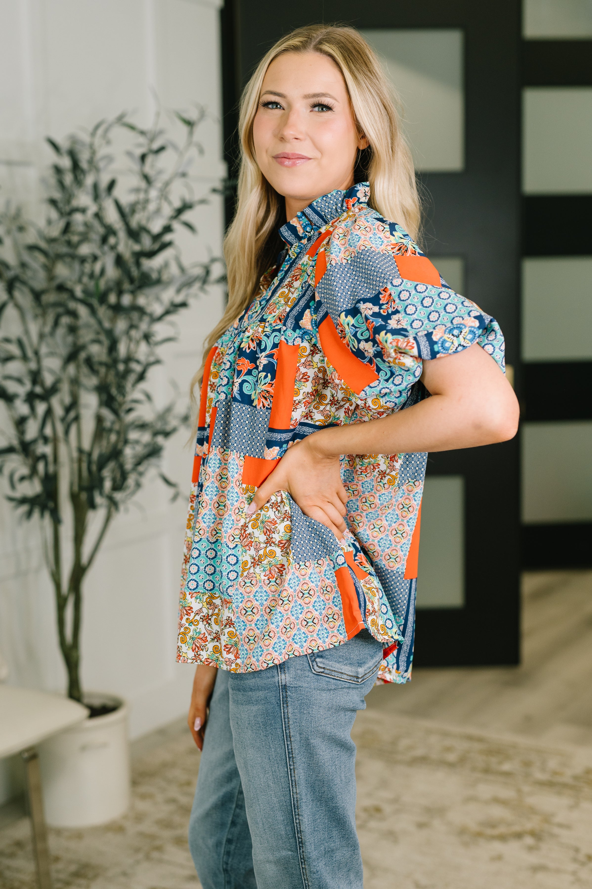 Woman wearing a blue patchwork blouse with puff sleeves and ruffle neckline with jeans indoors