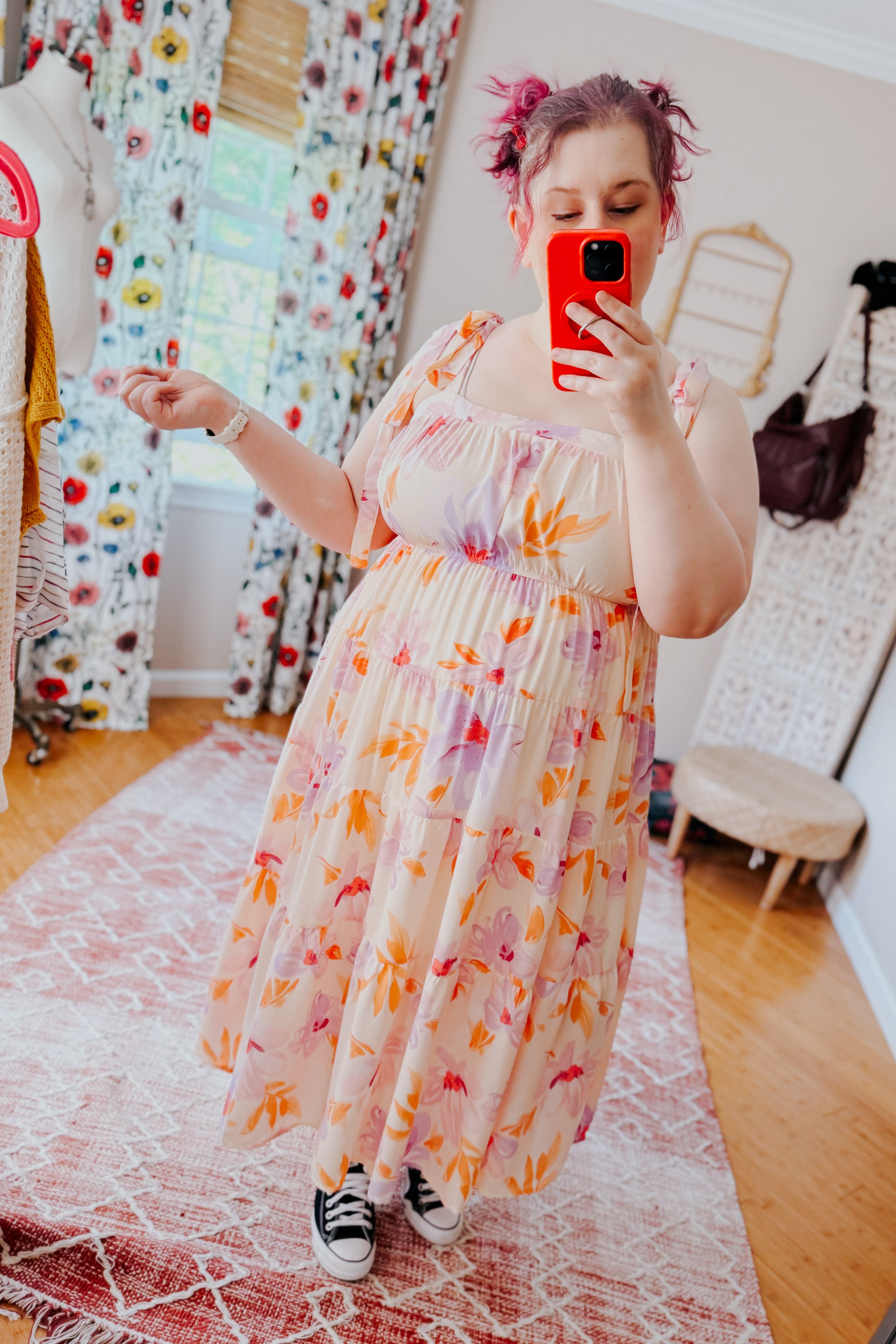 Plus-size woman with pink hair wearing peach floral tiered midi dress and black sneakers taking mirror selfie indoors
