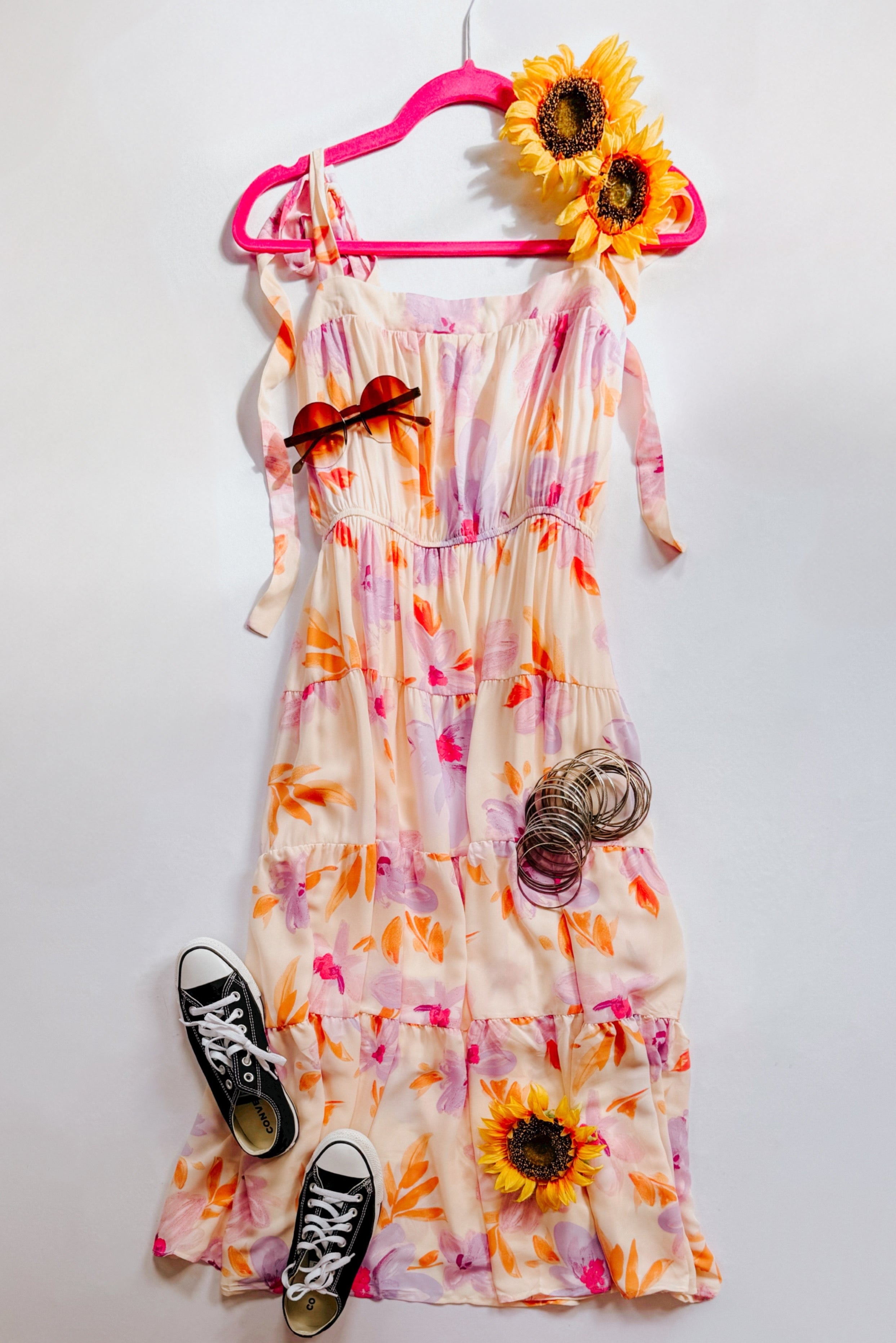 Peach pastel petals floral midi dress with tie straps styled with black sneakers, sunglasses, bracelets, and sunflowers