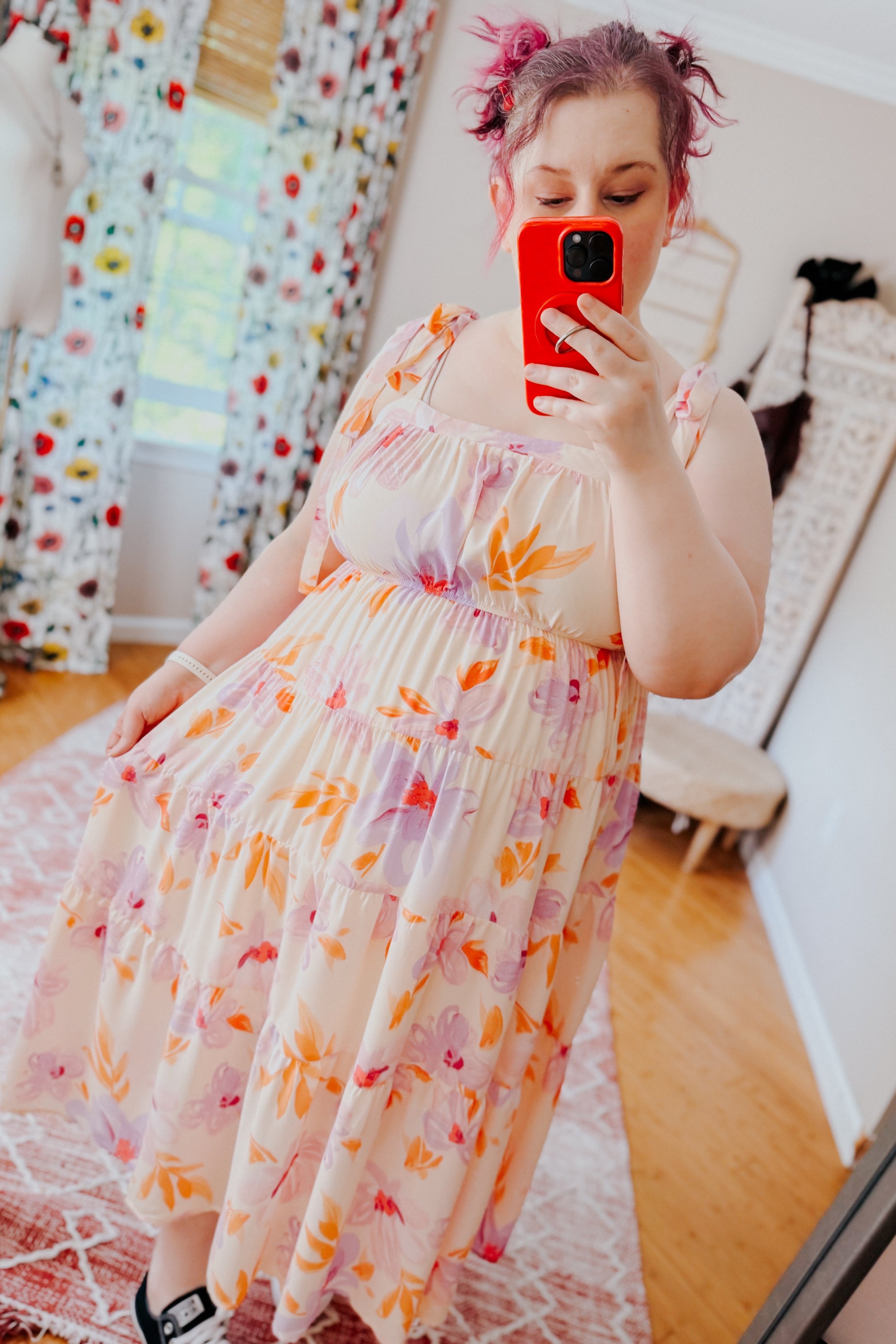 Plus-size woman with pink hair wearing pastel petals floral midi dress with adjustable shoulder ties taking selfie indoors