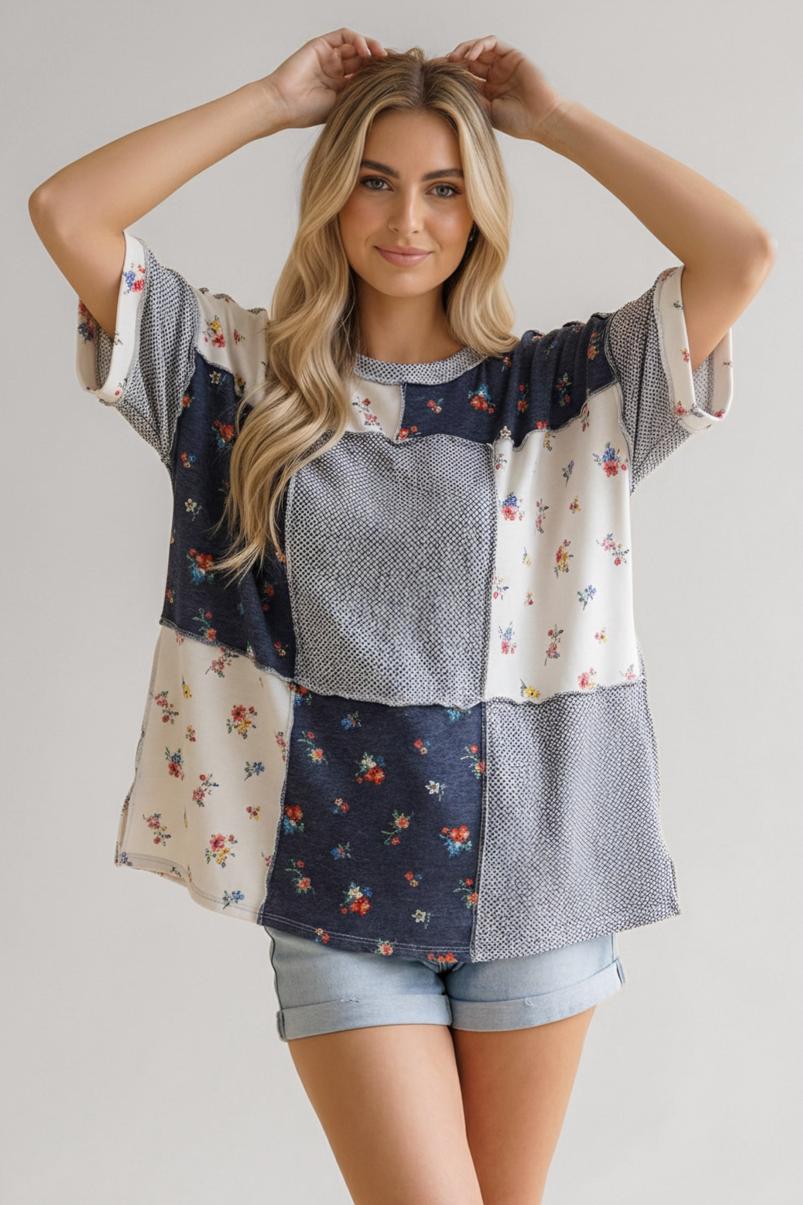 Woman wearing a loose patchwork top with navy and white floral prints paired with light denim shorts