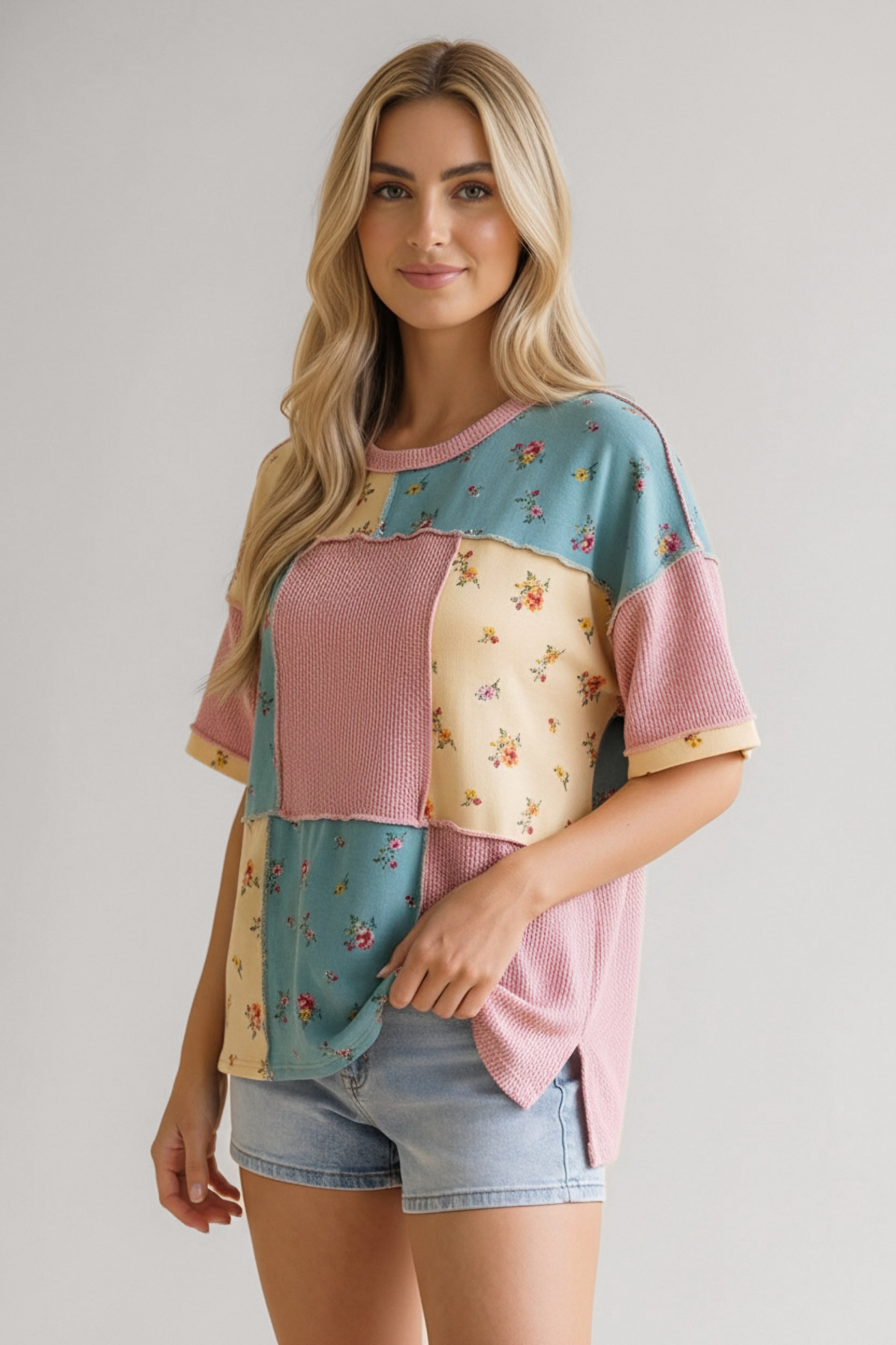 Woman wearing patchwork floral waffle knit top in pink, blue, and yellow paired with light denim shorts indoors