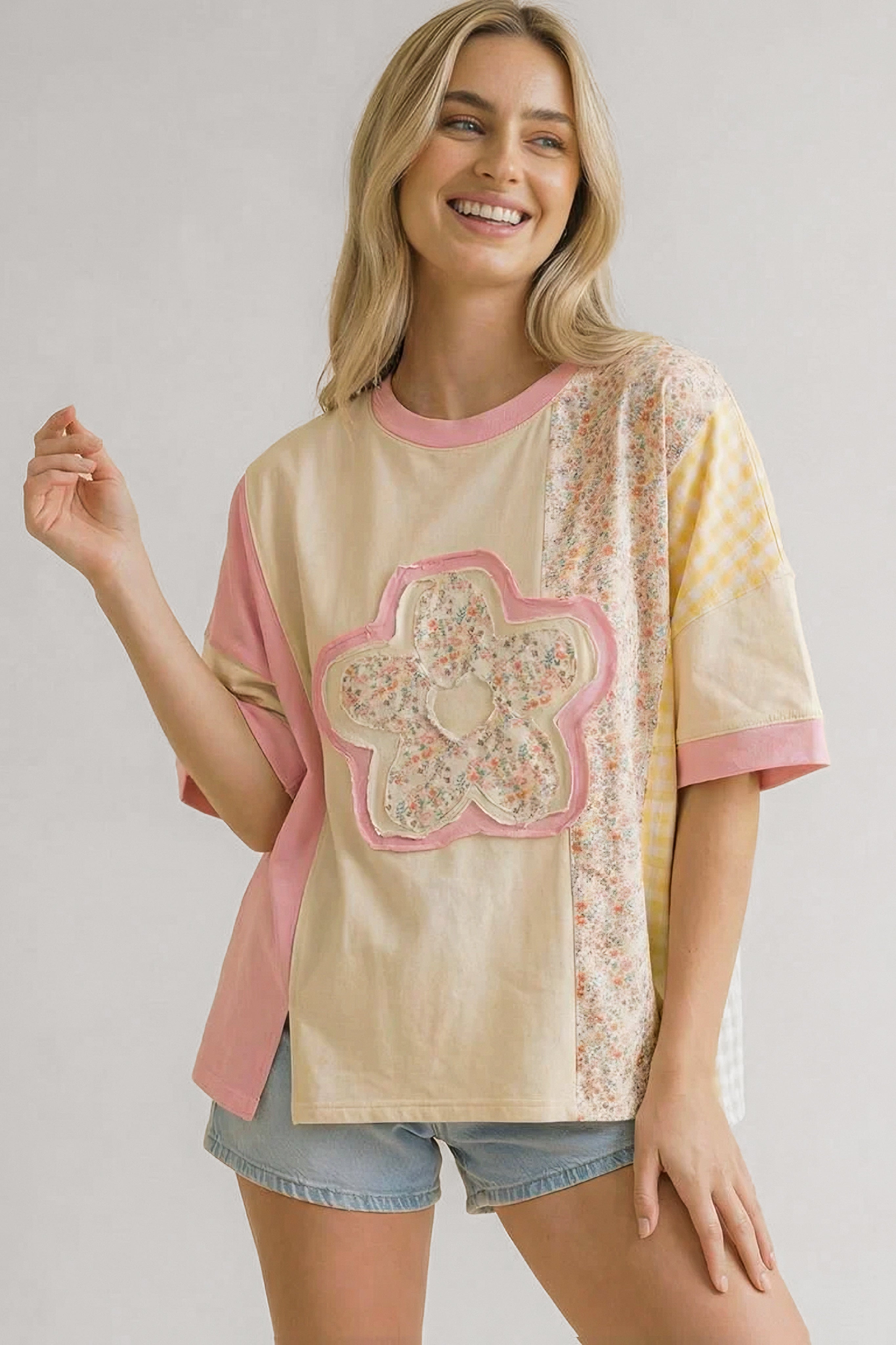 Smiling woman wearing a pink patchwork floral relaxed tee with mixed patterns paired with denim shorts indoors