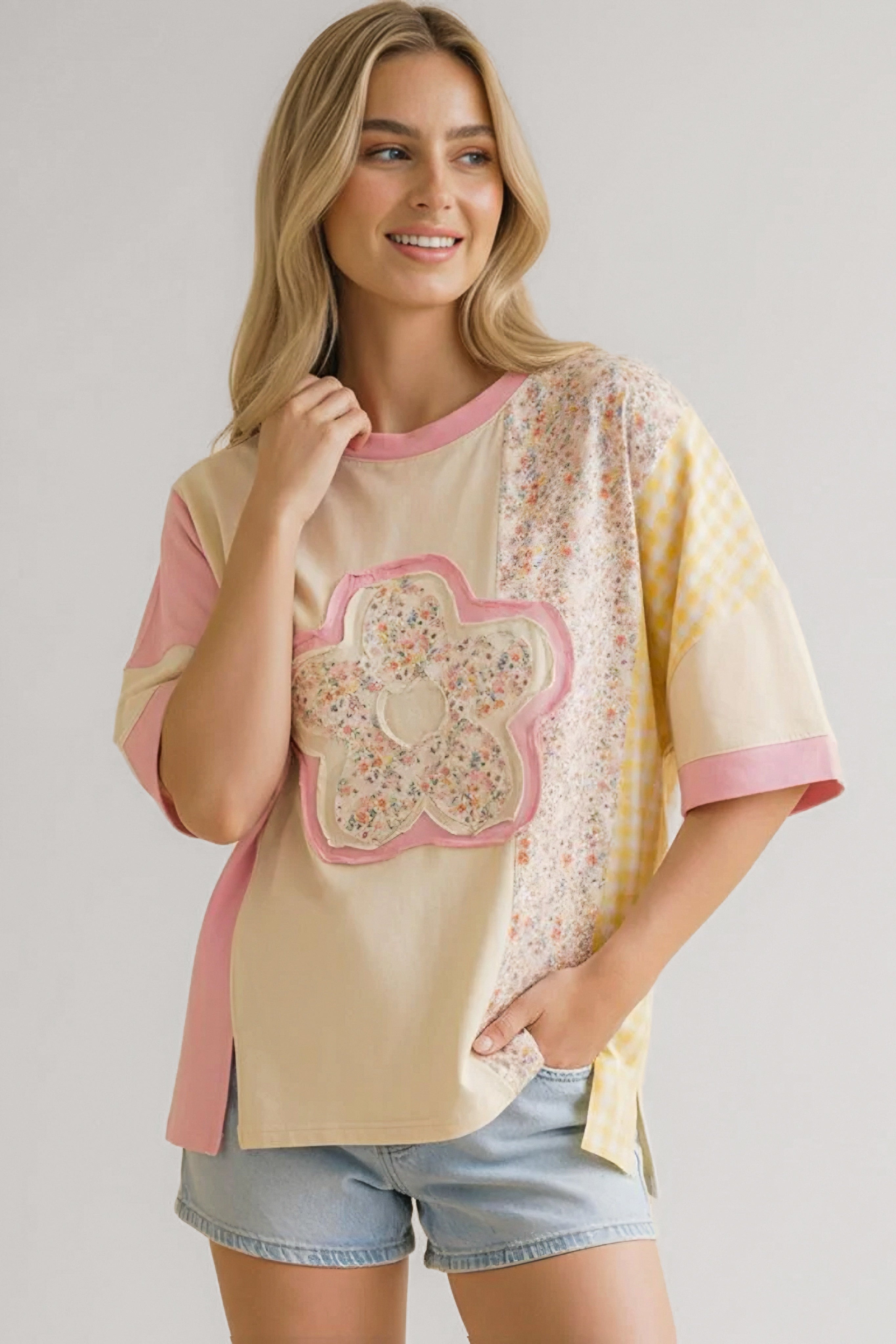 Woman wearing relaxed tee with patchwork floral and gingham patterns paired with light denim shorts smiling indoors