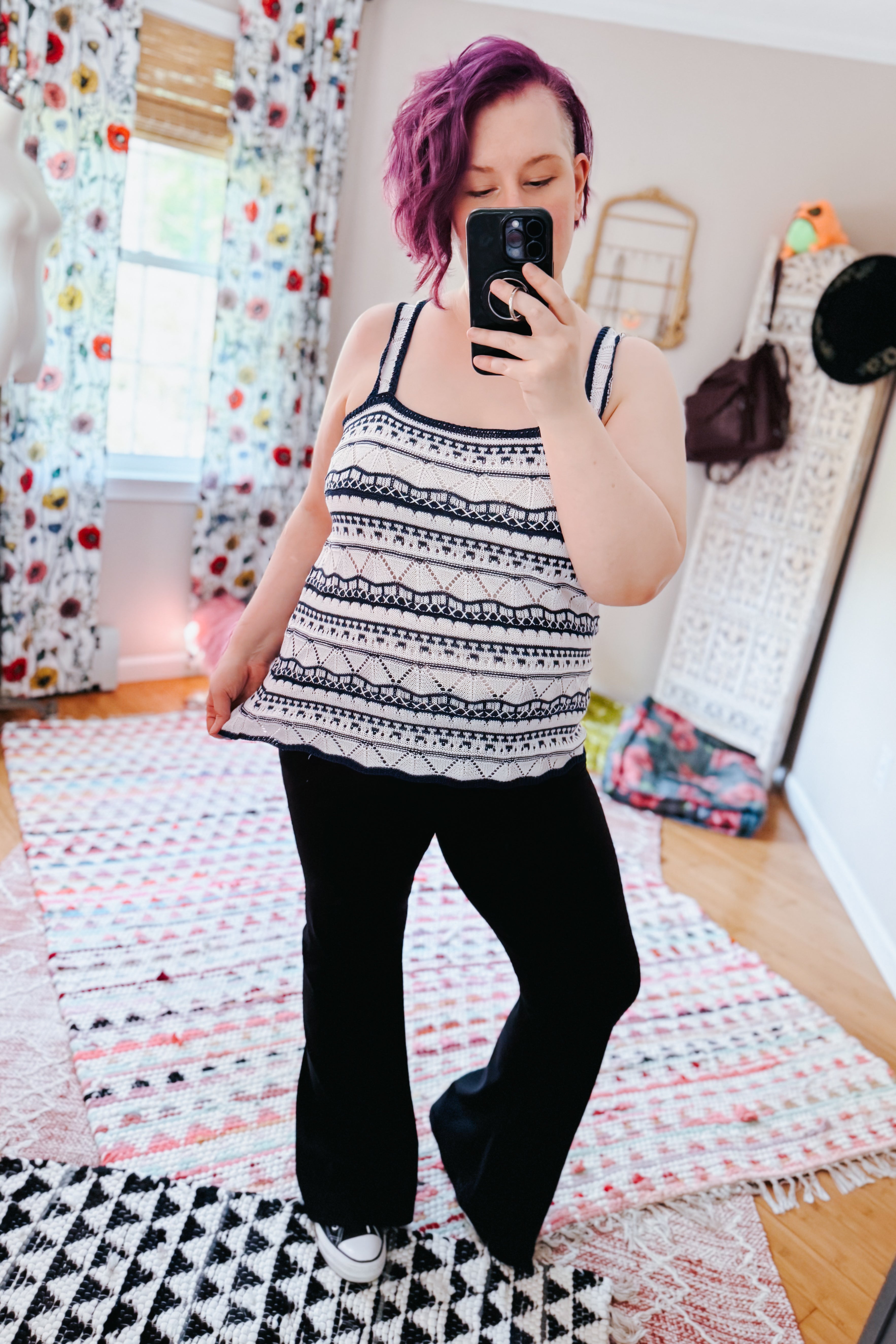 Woman with purple hair wearing a textured knit stripe sweater tank and black pants in a cozy, eclectic style setting