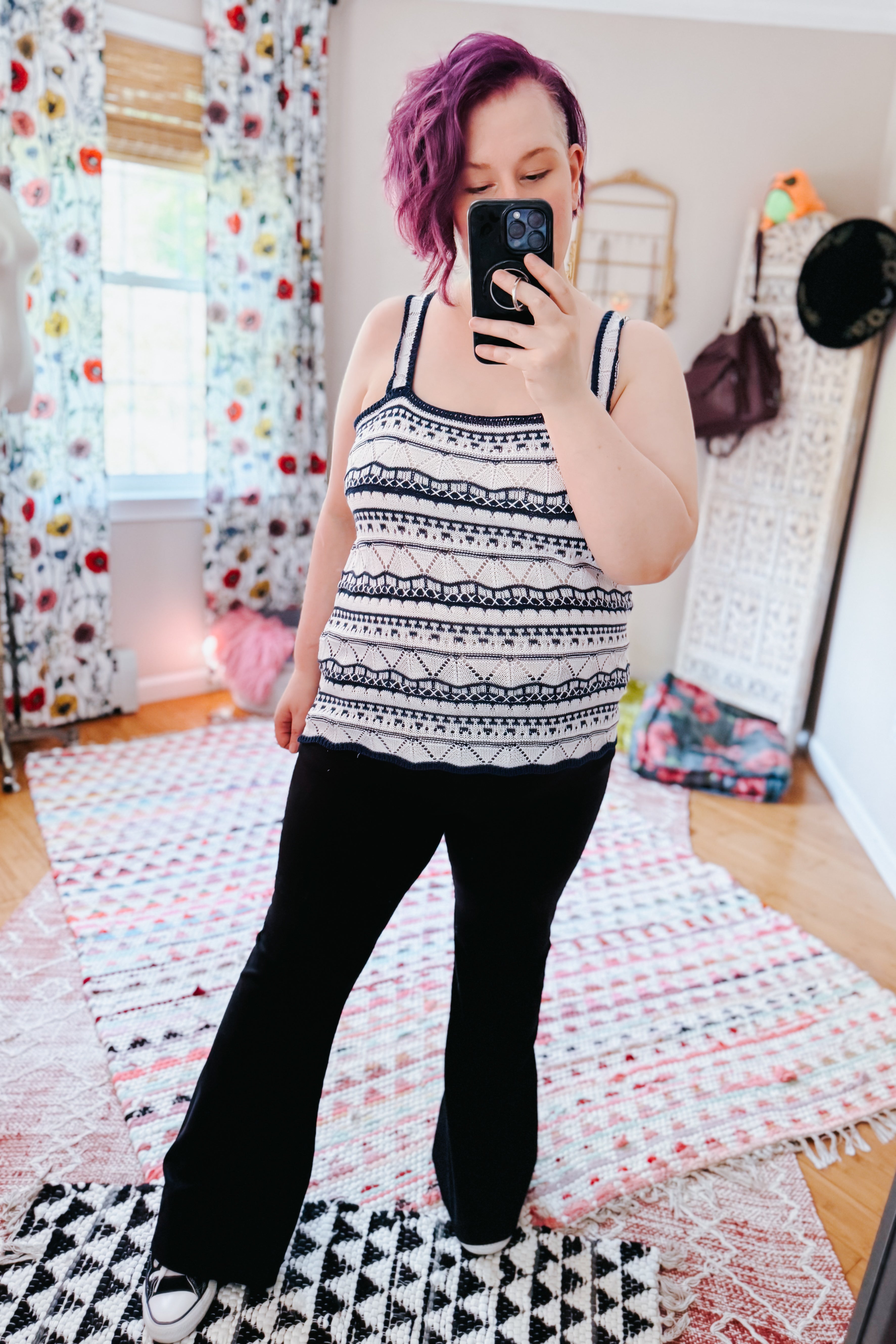 Woman wearing a black and white patterned sleeveless sweater tank with scalloped trim in a bold, eclectic setting
