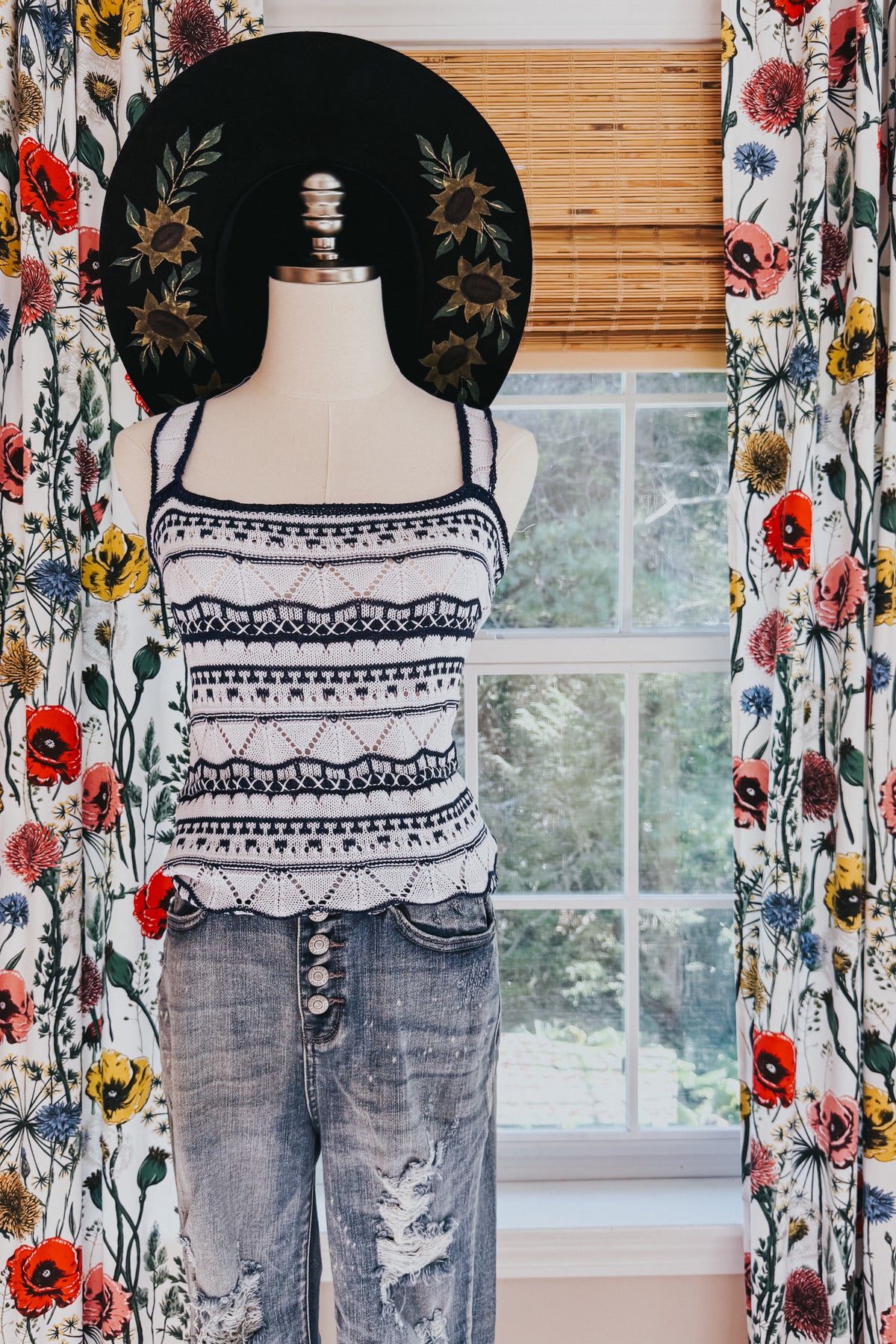 Mannequin wearing a blue pointelle knit sweater tank with patterned stripes and scalloped trim paired with distressed button fly jeans indoors