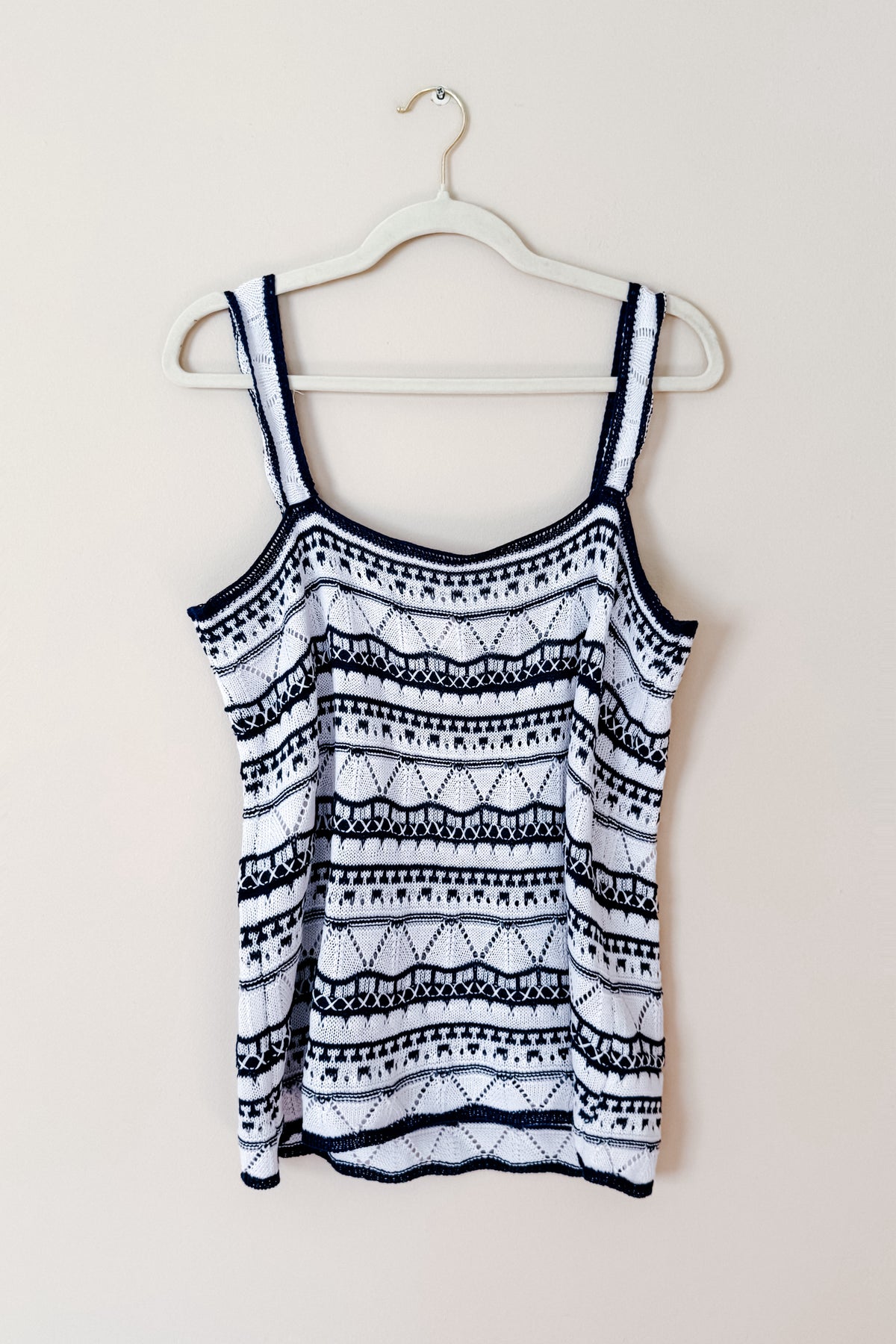 Blue and white pointelle knit sweater tank with scalloped trim and contrasting geometric stripe pattern hanging on a hanger