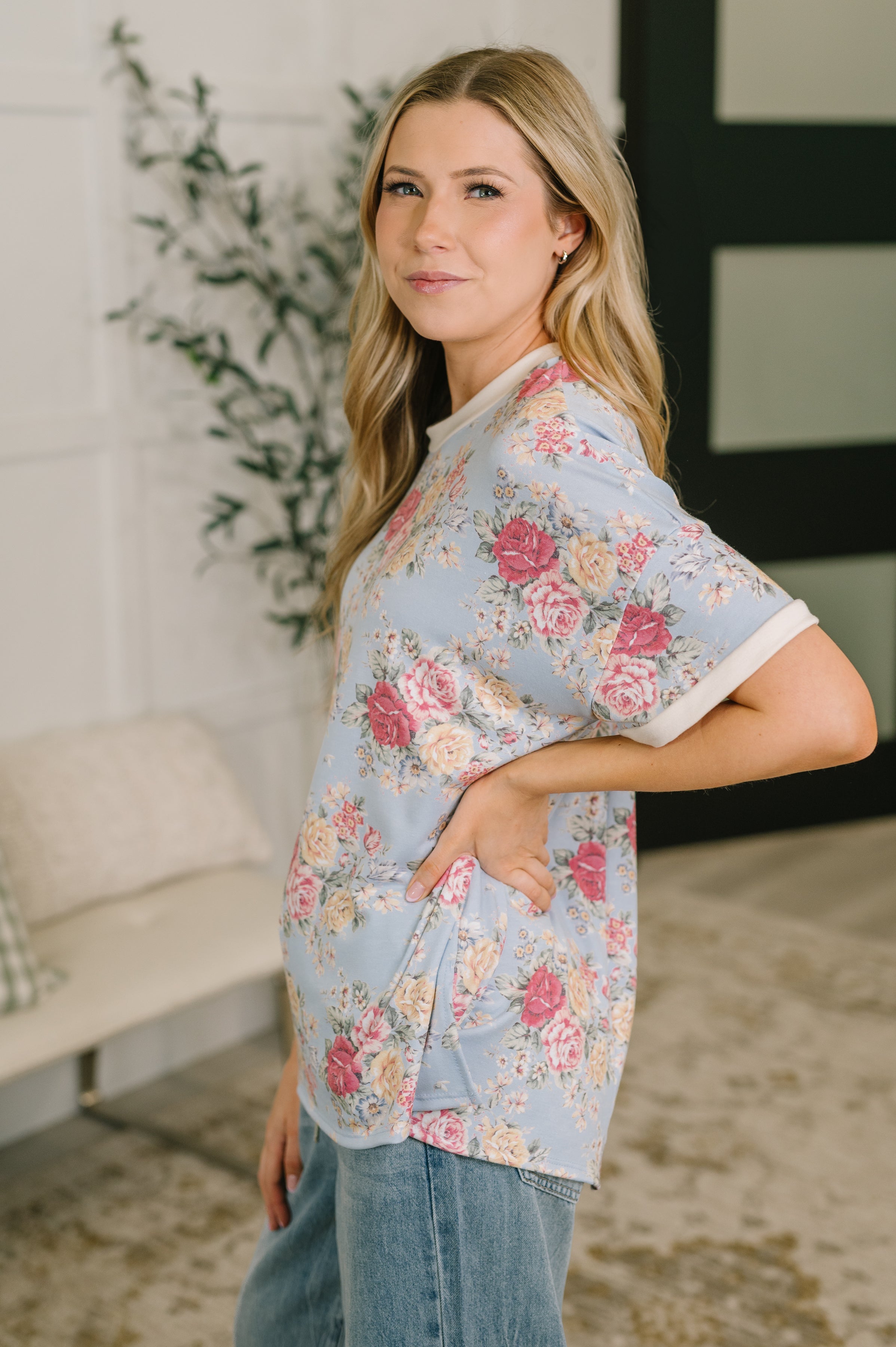 Woman wearing blue relaxed floral print tee with rolled sleeves paired with casual jeans in cozy indoor space