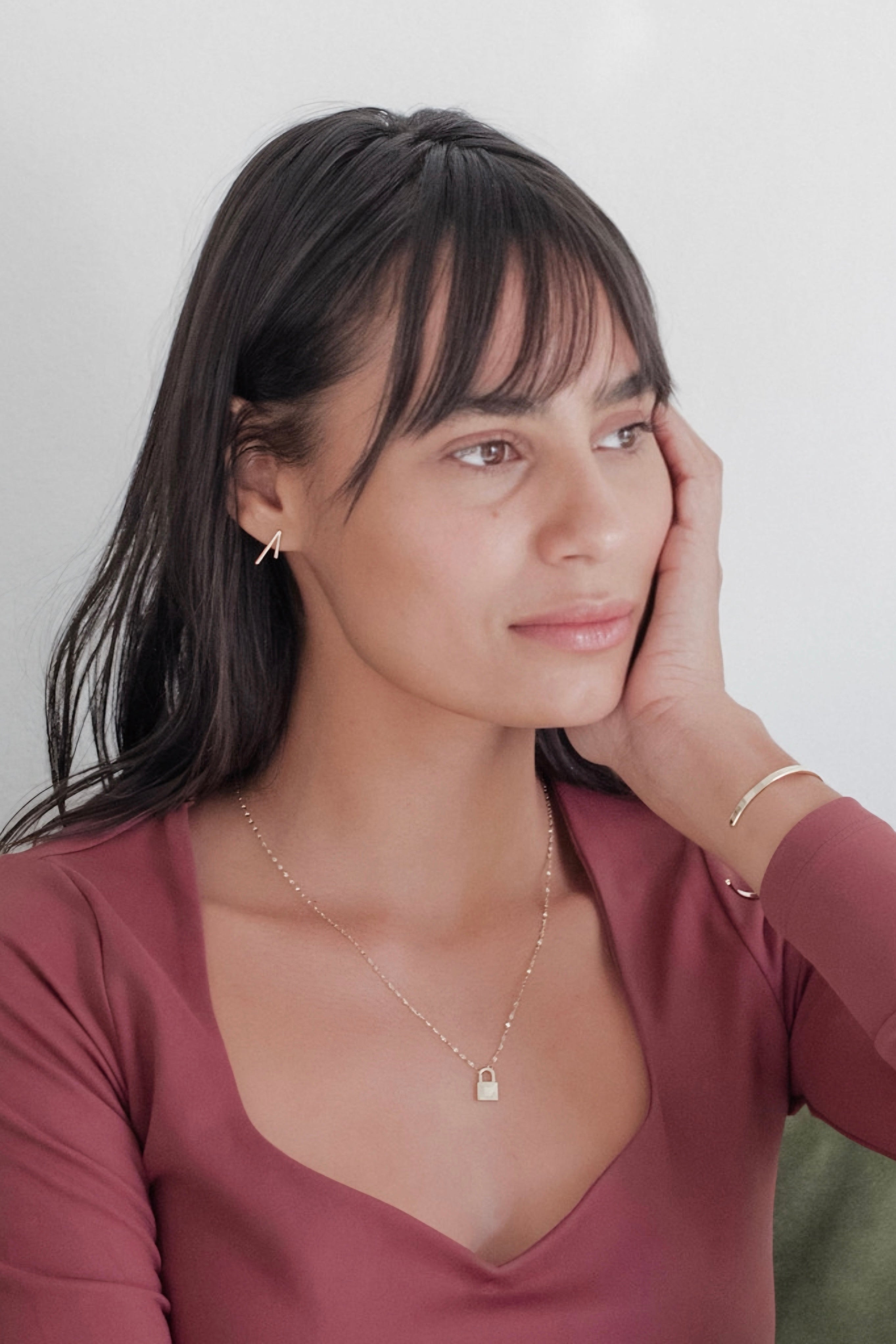 Woman wearing gold lock pendant necklace and matching bracelet with sleek earrings in casual mauve top