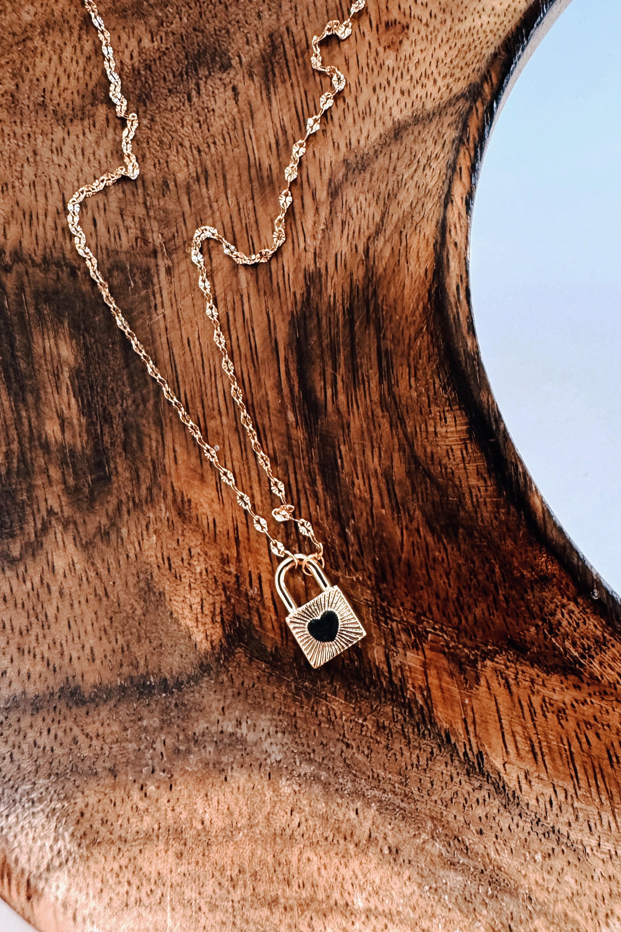 Gold chain featuring a small padlock pendant with heart detail resting on textured wooden surface in bold style