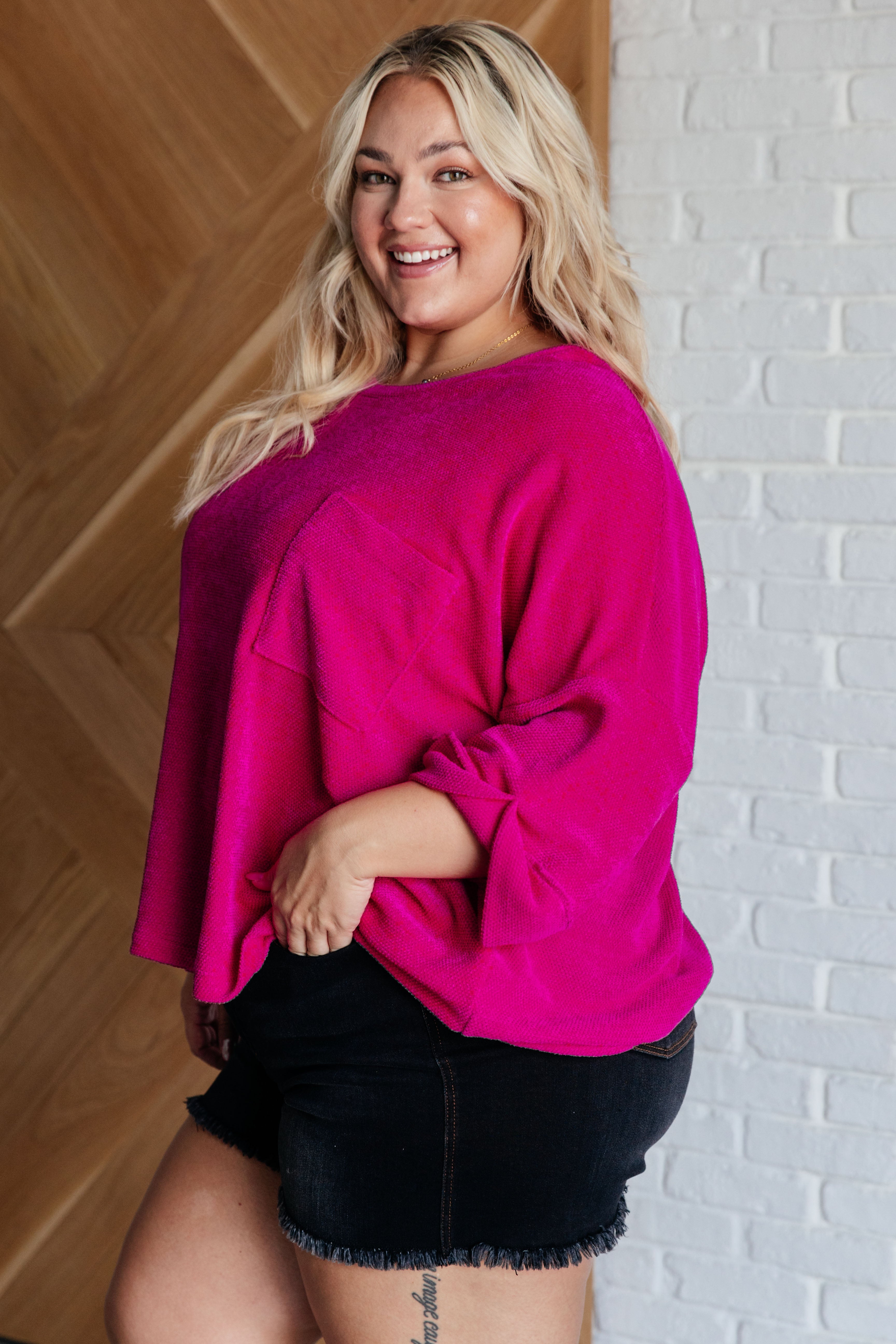 Plus-size model wearing vibrant fuchsia plush blouse with rolled sleeves and front pocket in eclectic, size-inclusive style