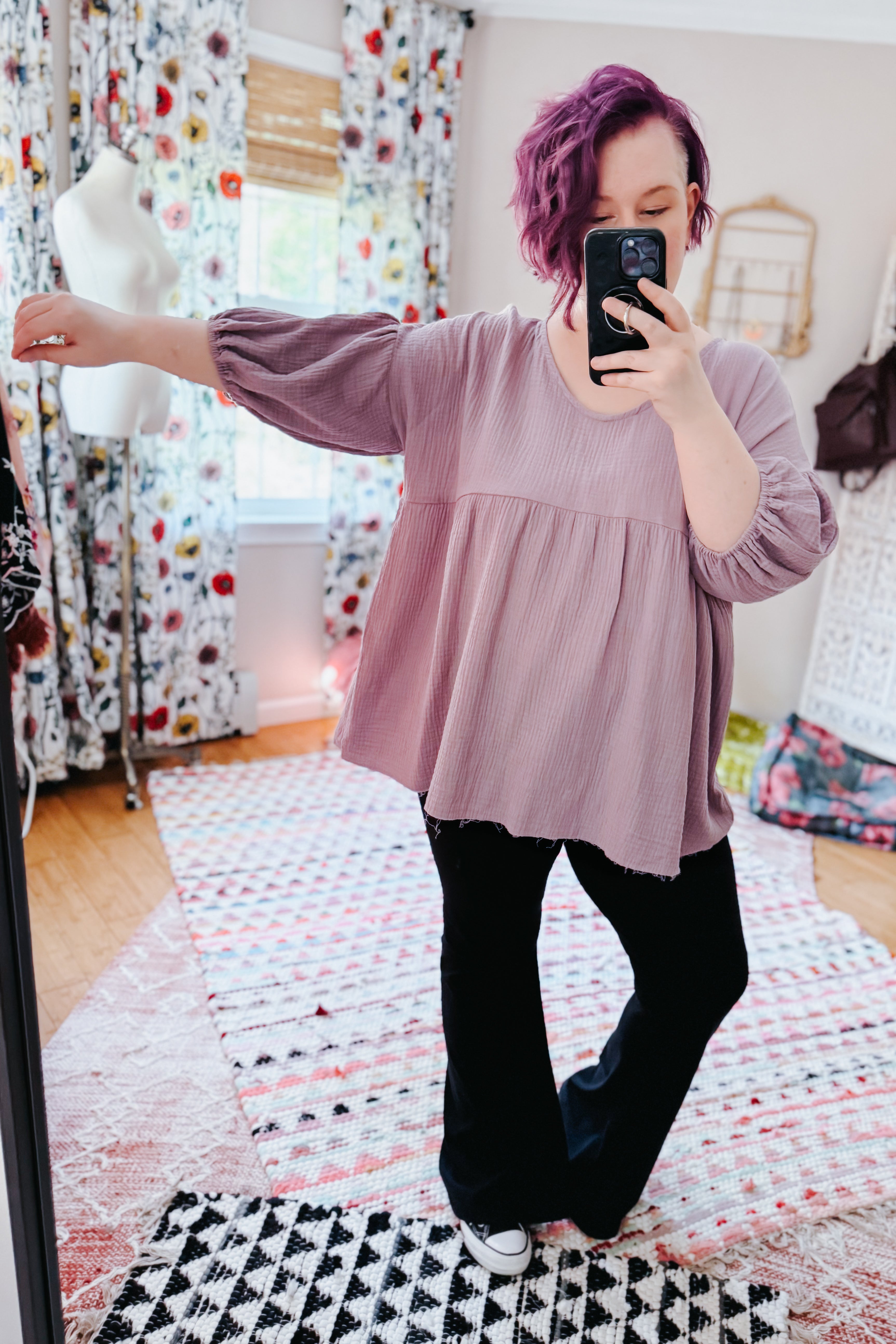 Woman with purple hair wearing a soft purple bubble sleeve peasant blouse and black pants in an eclectic, free-spirited room