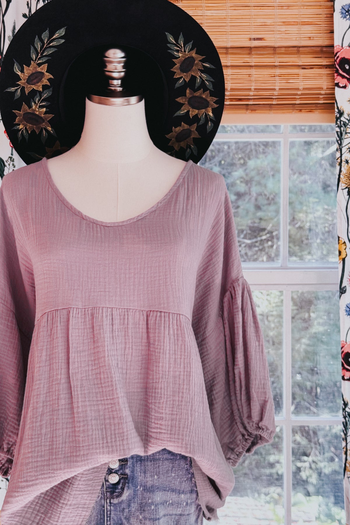 Purple gauze peasant blouse with balloon sleeves and babydoll silhouette displayed on a mannequin with distressed jeans and a floral hat
