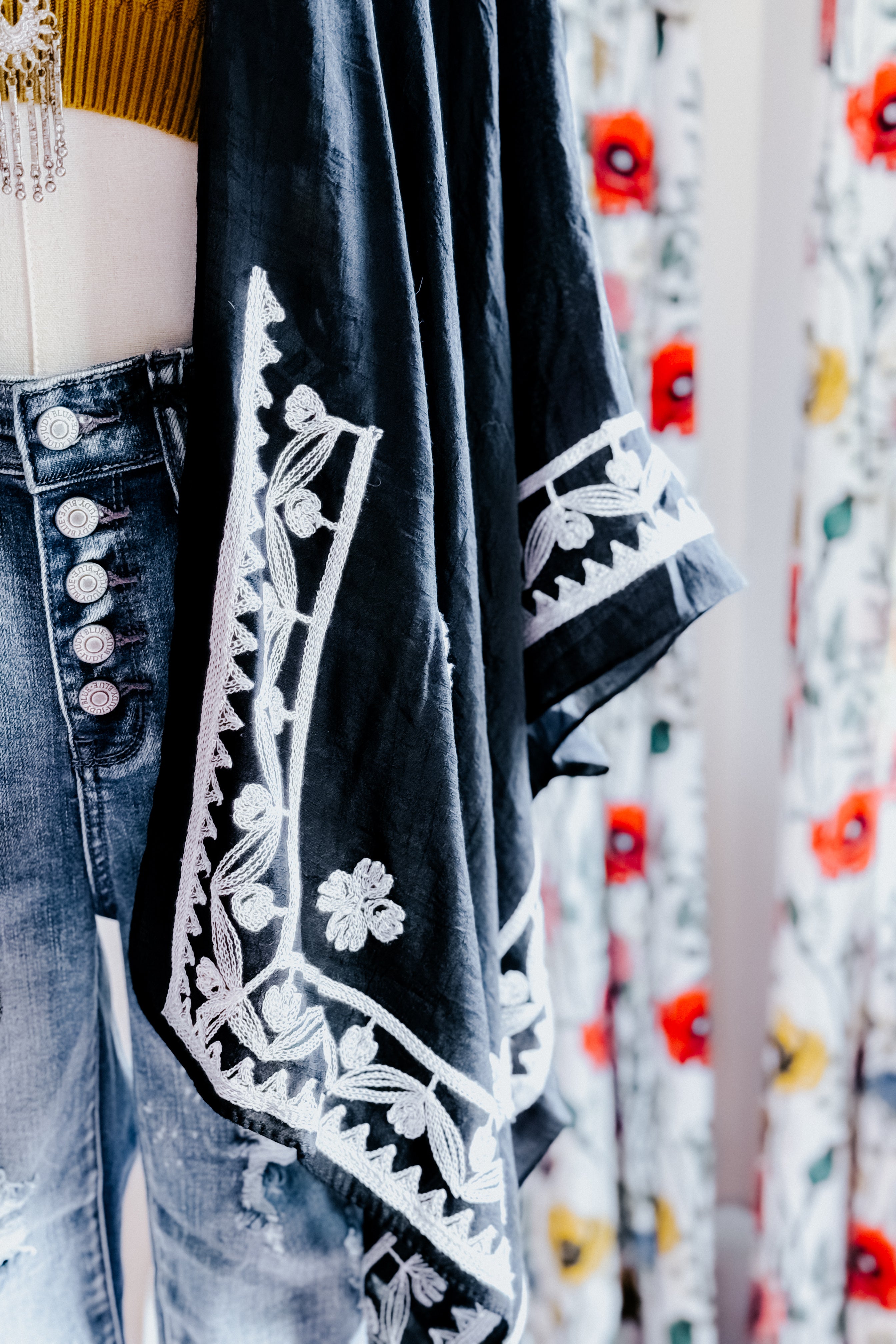 Black layering piece with white floral embroidery draped over high-waisted denim jeans in eclectic, bold style