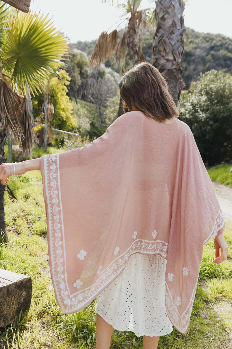 Woman wearing blush taupe layering piece with delicate white poppy embroidery in free spirited, eclectic outdoor setting