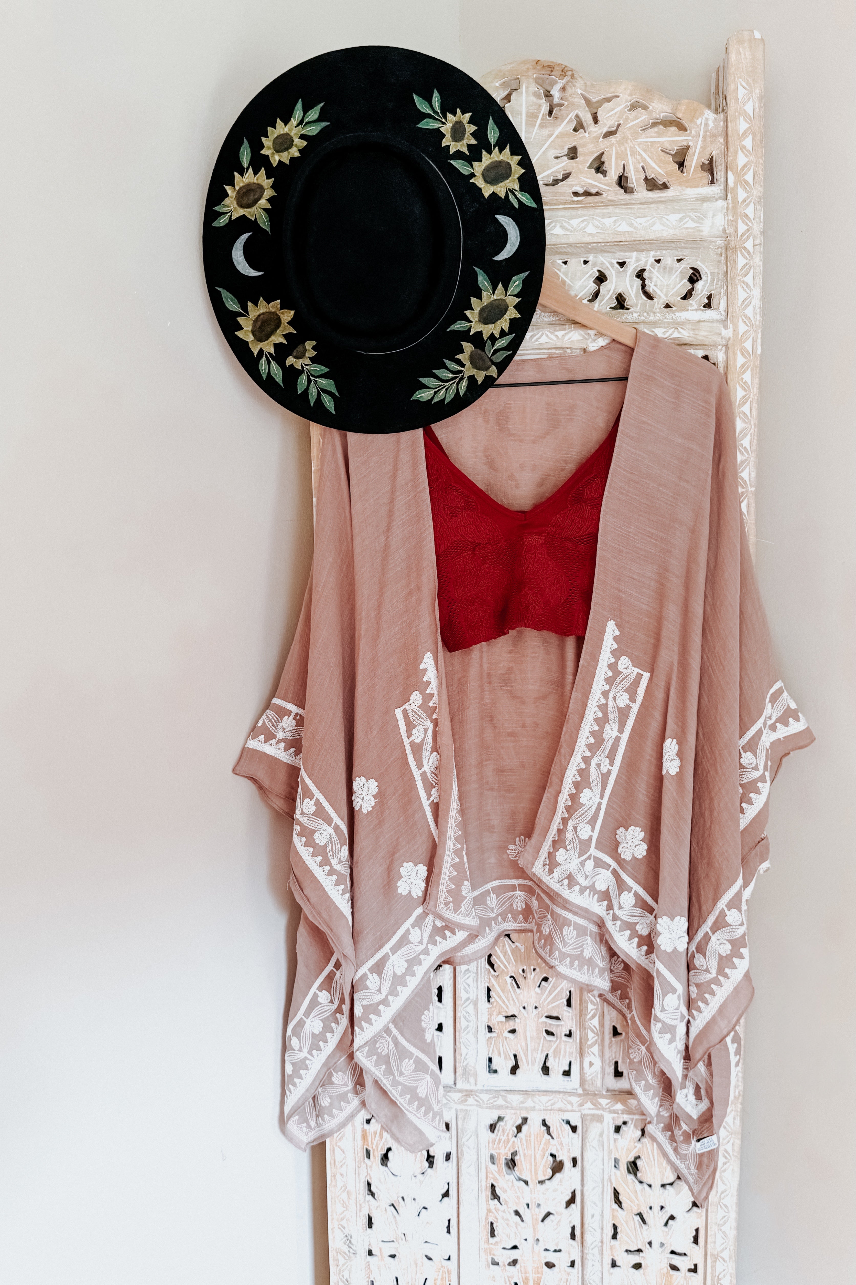 Blush taupe embroidered layering piece with white floral trim paired with red lace top and black sunflower-printed hat in eclectic style