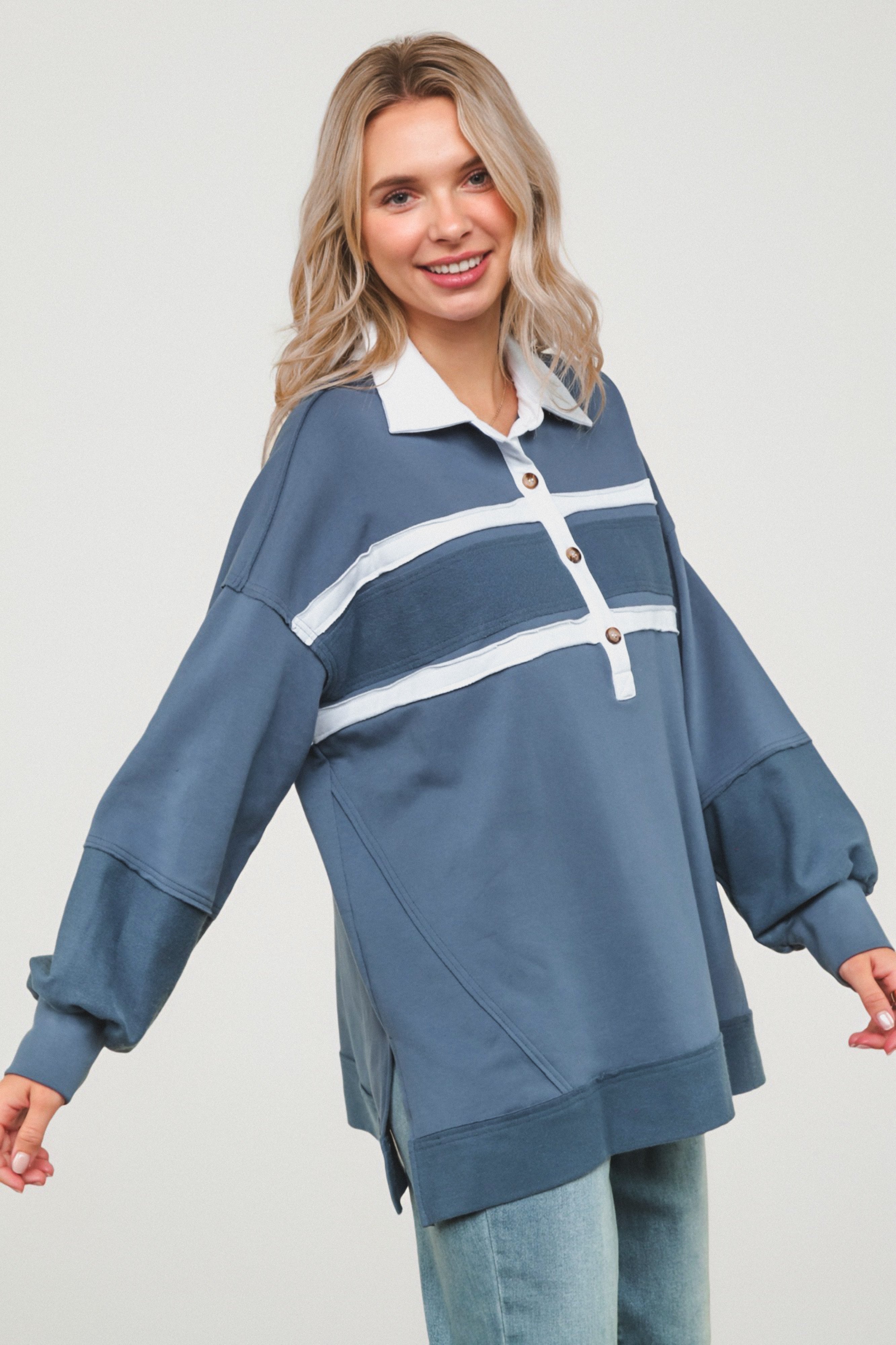 Woman wearing relaxed slate blue polo top with white stripes and wooden buttons, paired with light wash denim jeans