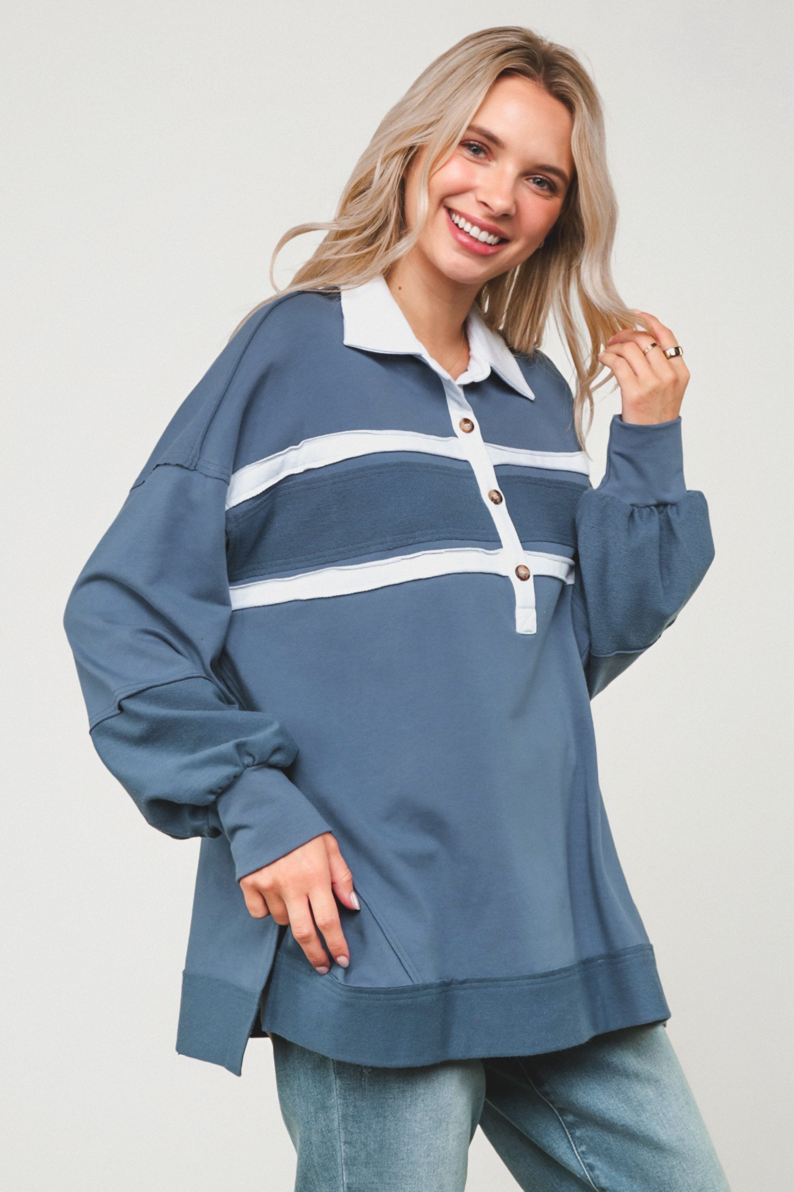 Smiling woman in relaxed steel blue polo top with white stripes and wooden buttons, paired with light wash jeans