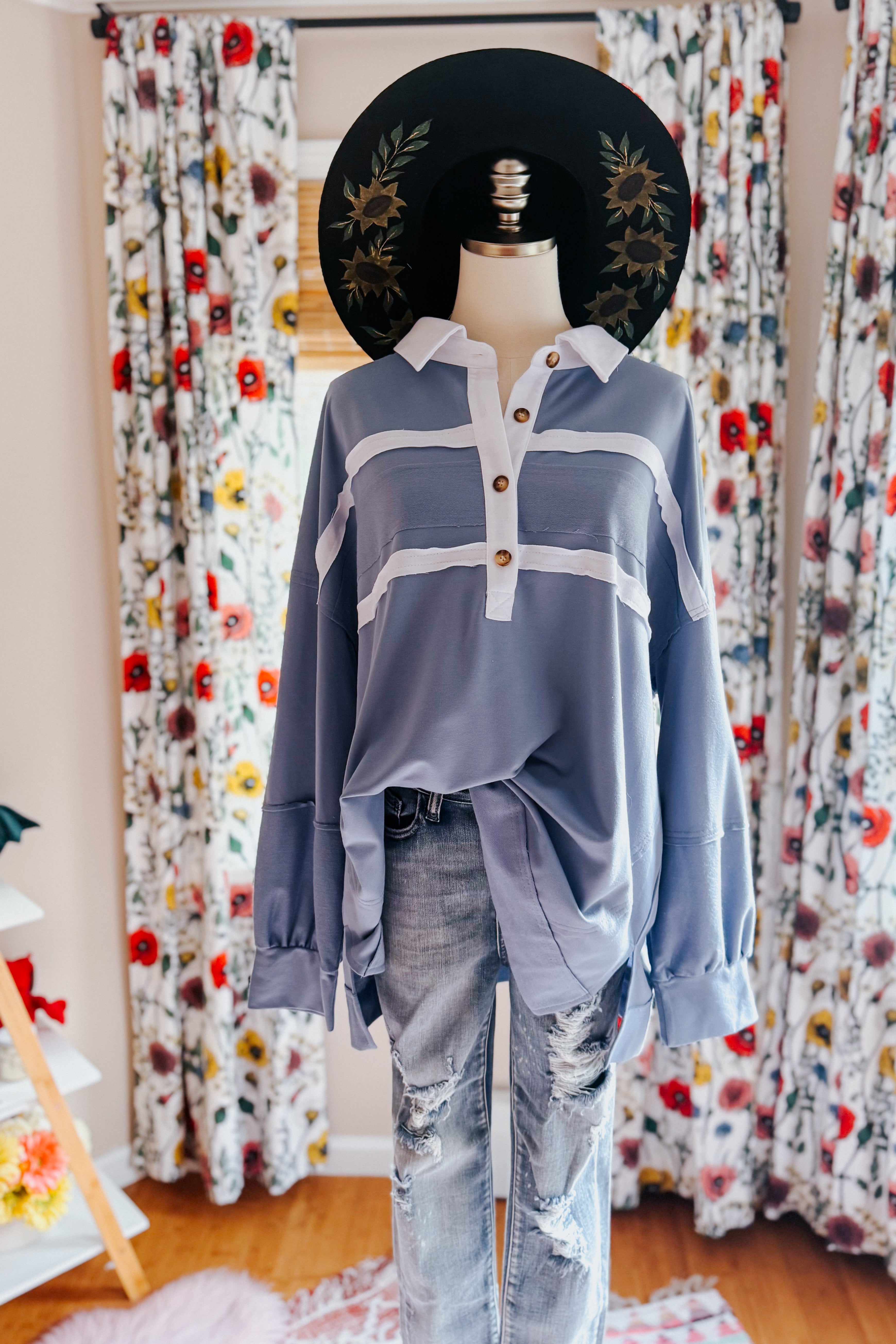 Mannequin dressed in slate blue long-sleeve polo with white stripes, wooden buttons, paired with distressed jeans and black hat