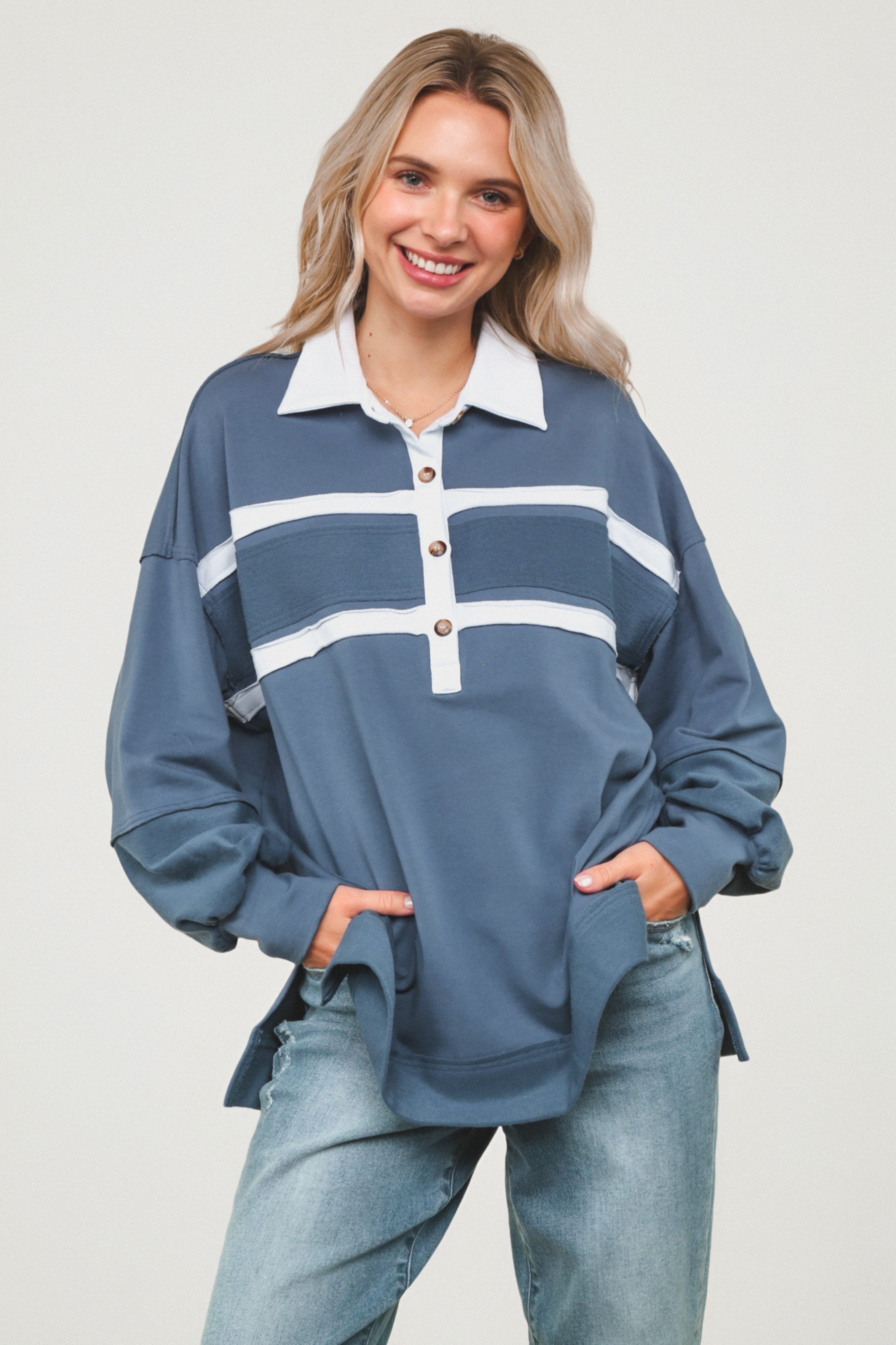 Smiling woman wearing loose steel blue polo top with white collar and stripes paired with casual light wash jeans