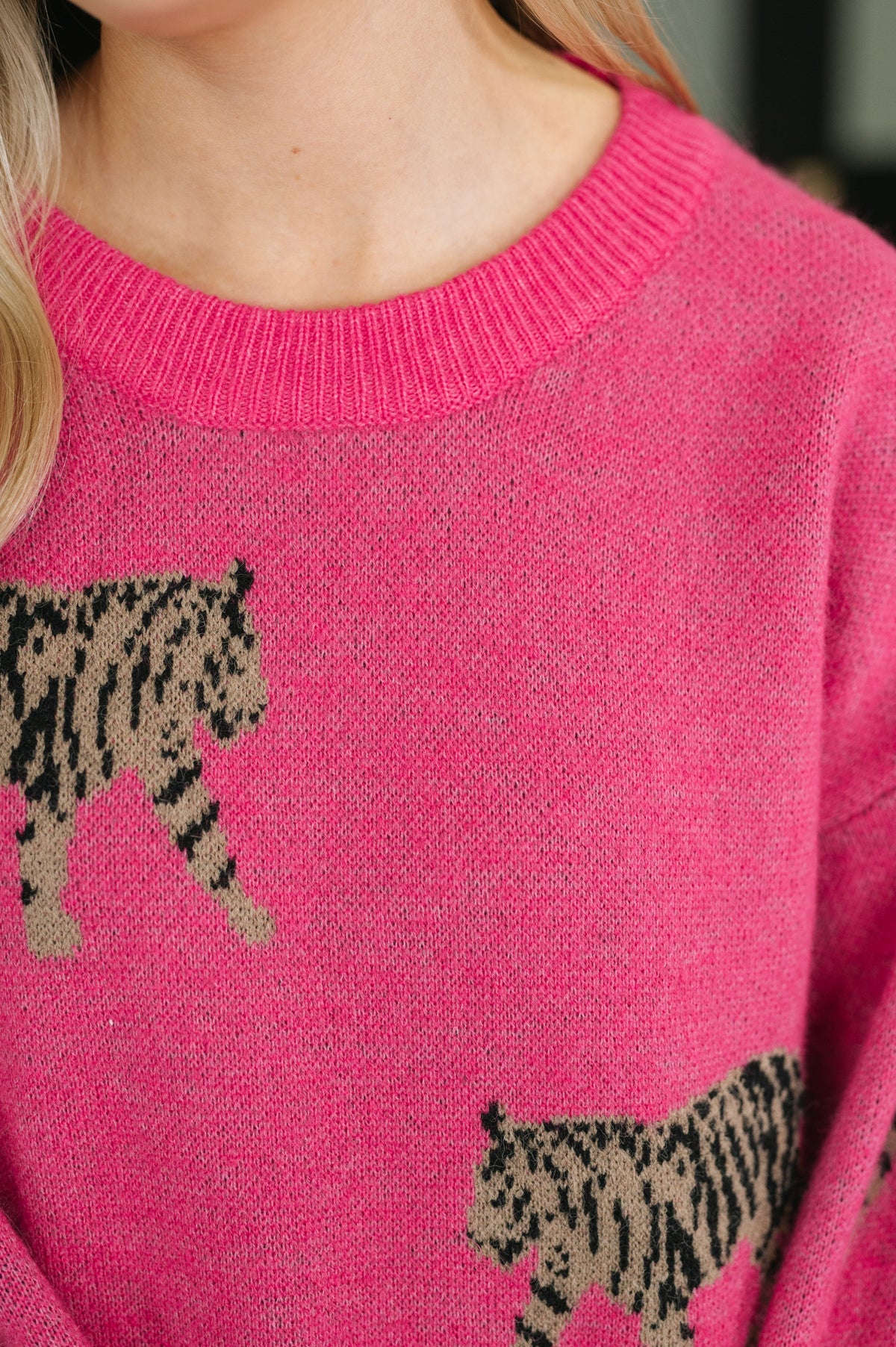 Close up of a woman wearing a pink knit pullover with a ribbed crew neckline and bold prowling animal graphics