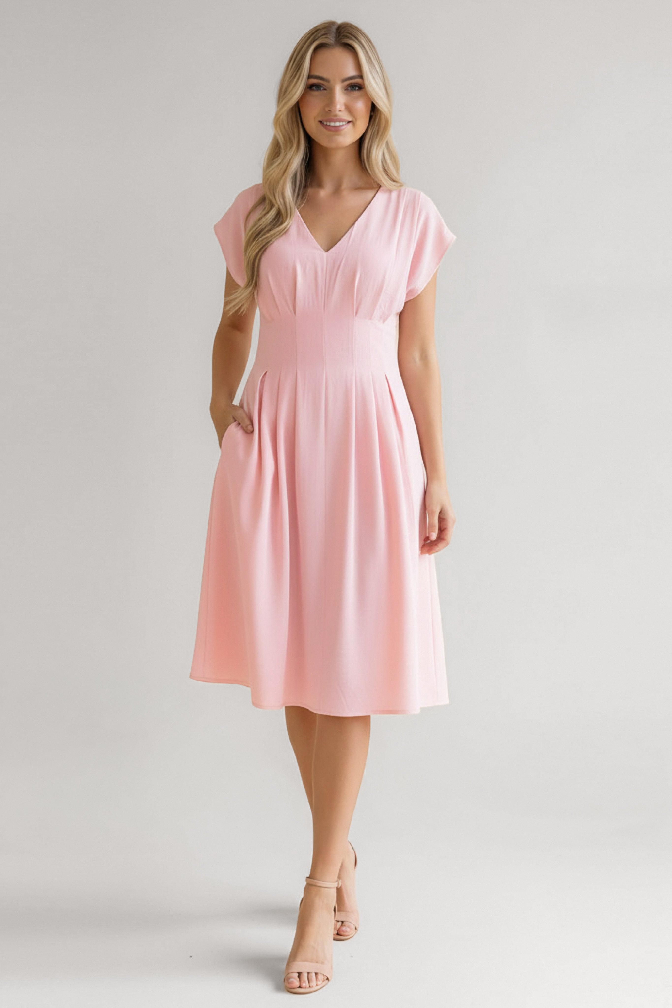 Woman wearing a soft pink midi dress with cap sleeves, a fitted waist, and pleated skirt paired with nude heels