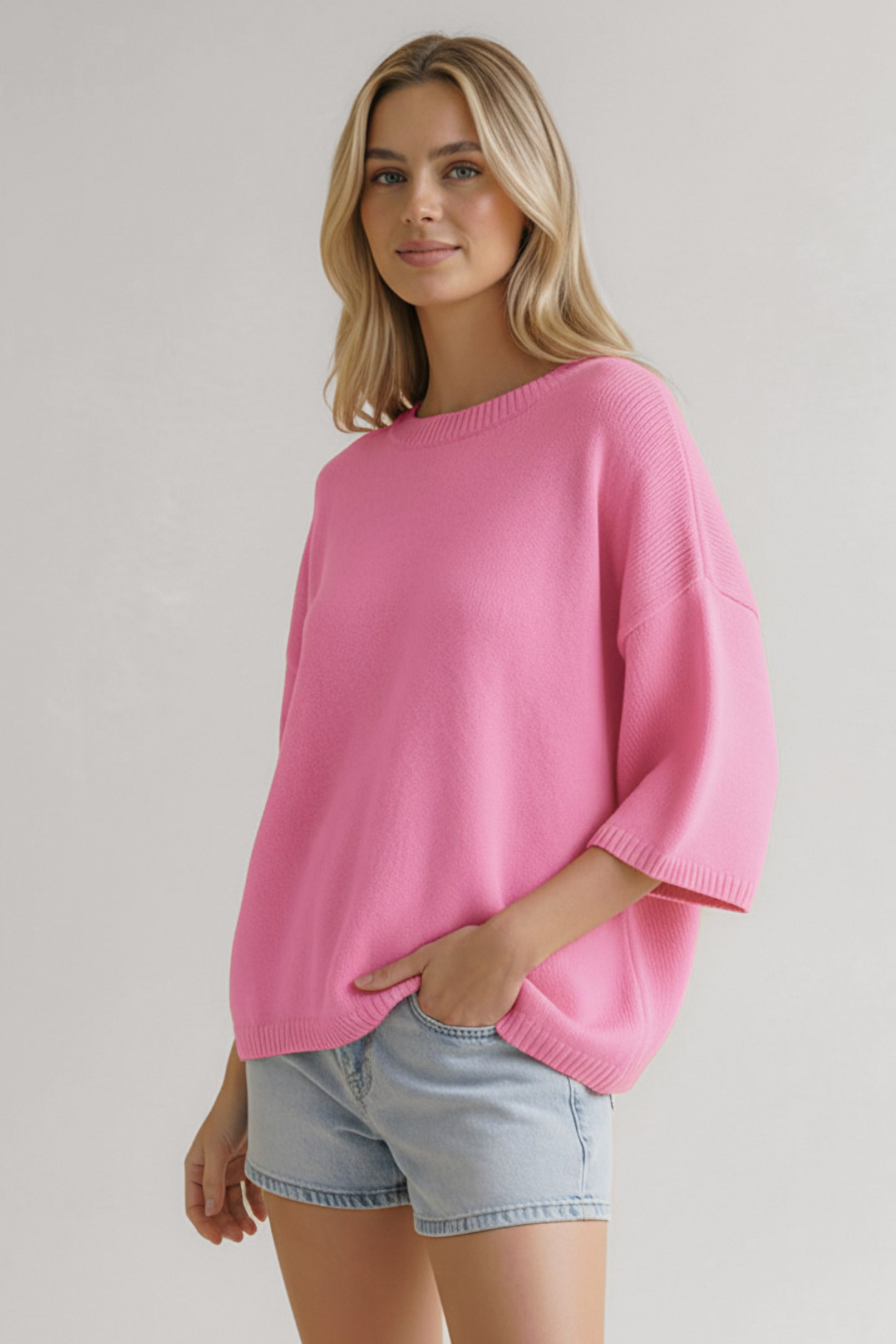 Woman wearing loose pink knit sweater tee paired with light denim shorts against a plain background
