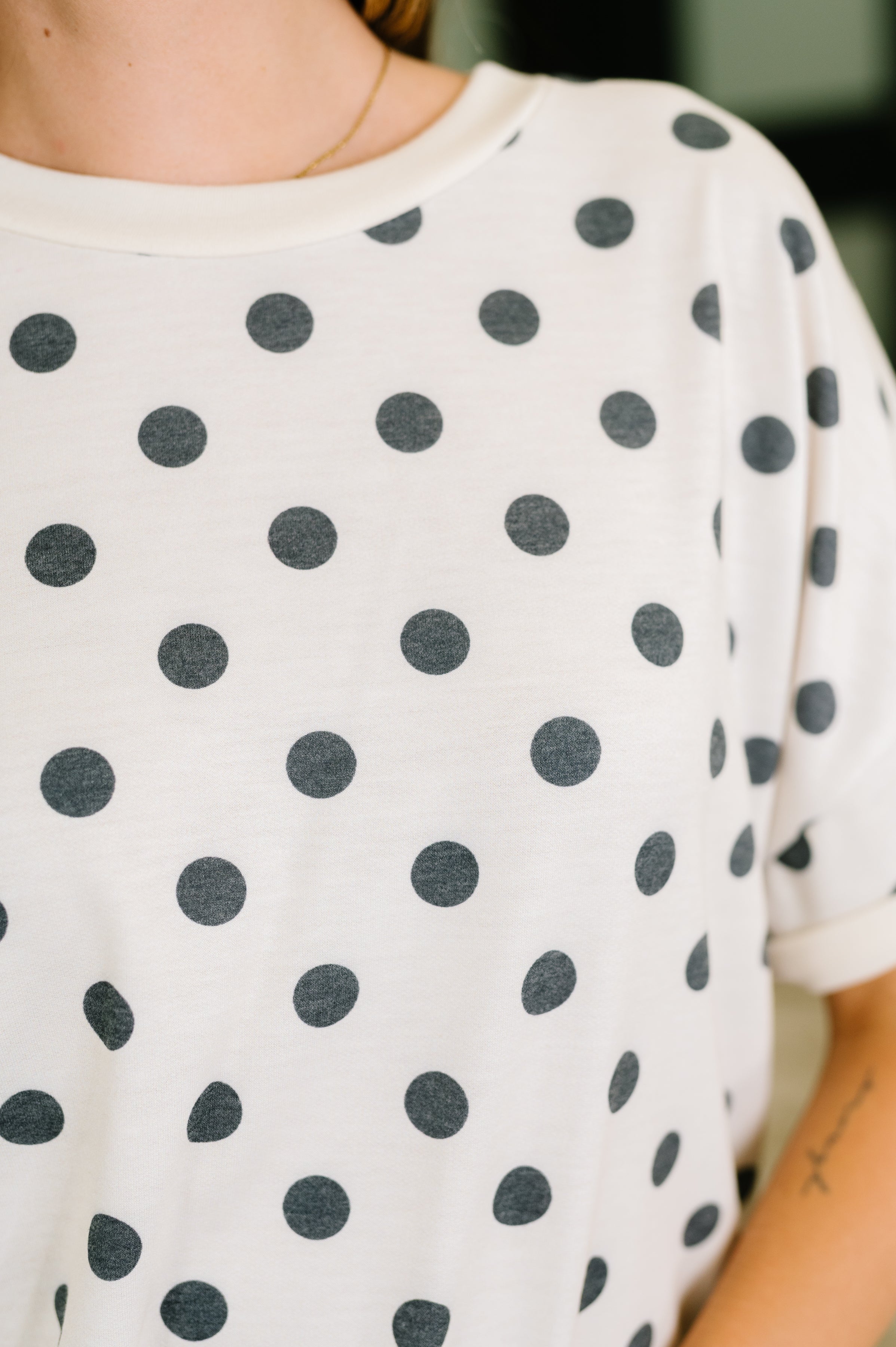 Close-up of ivory oversized tee with black polka dots and drop shoulder seam on model’s upper torso and arm