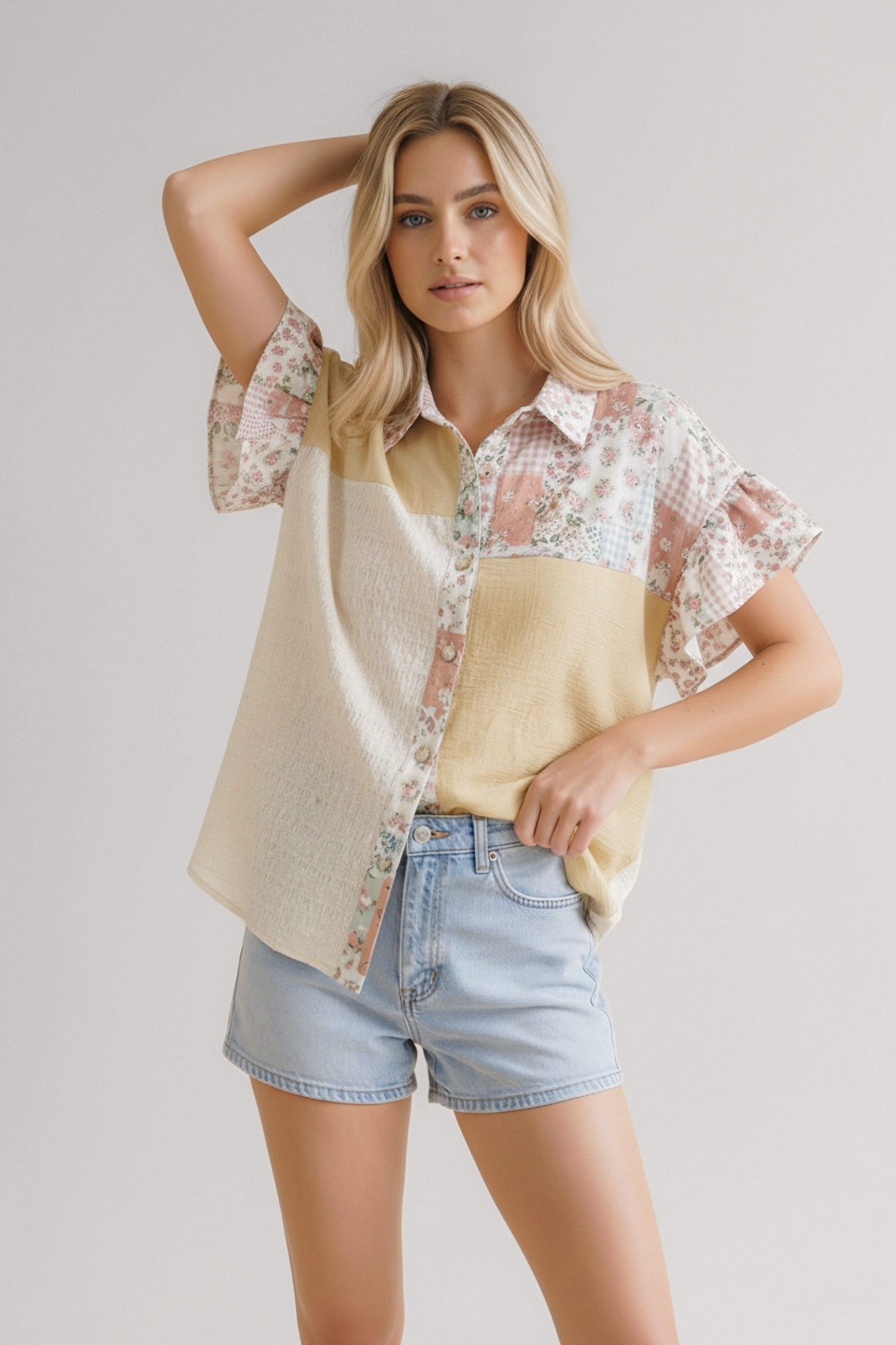 Woman wearing beige patchwork floral button-down top with short flutter sleeves paired with light denim shorts