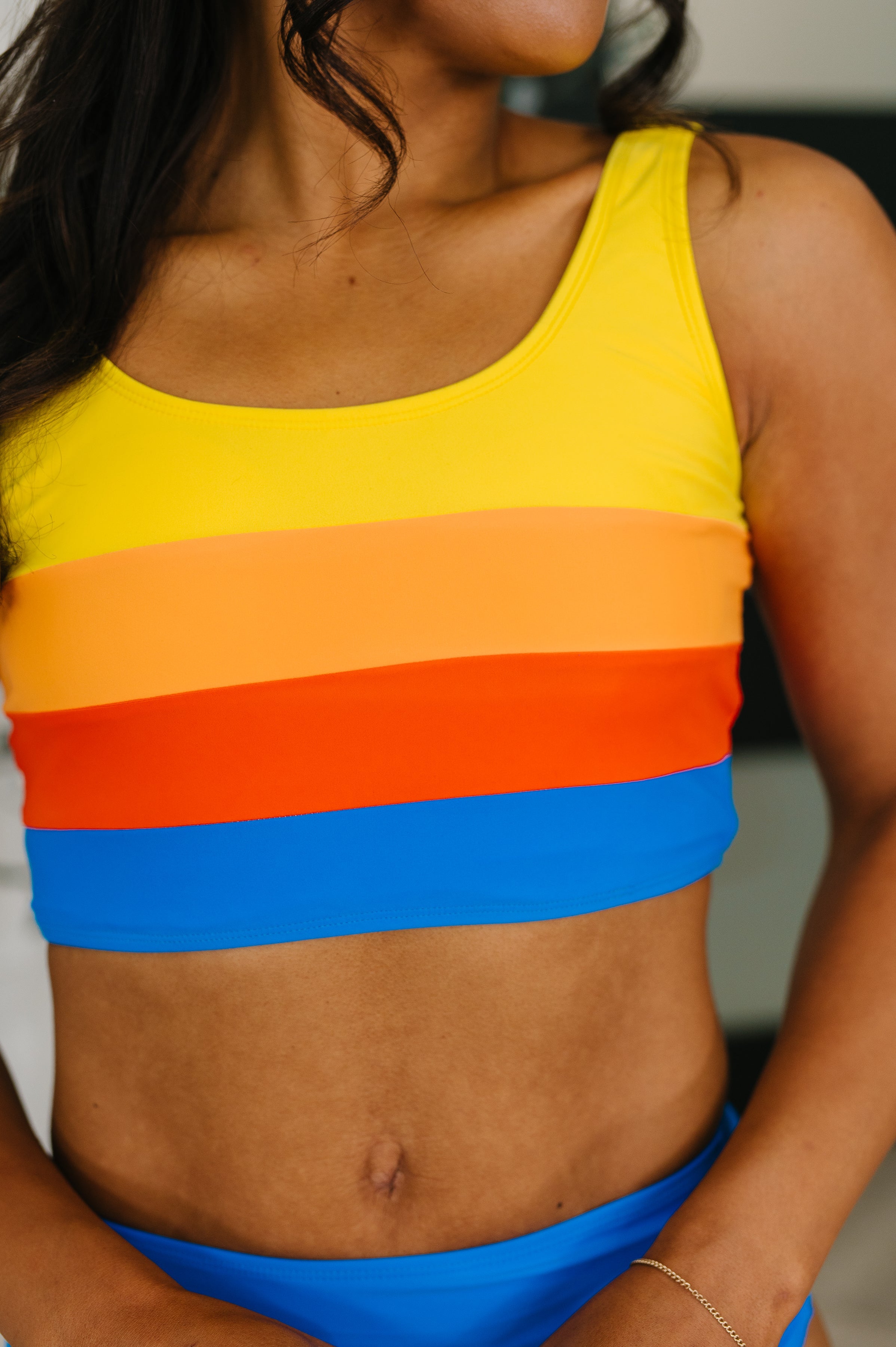 Close-up of color-blocked ruched swim top in yellow, orange, red, and blue on model with smooth skin indoors