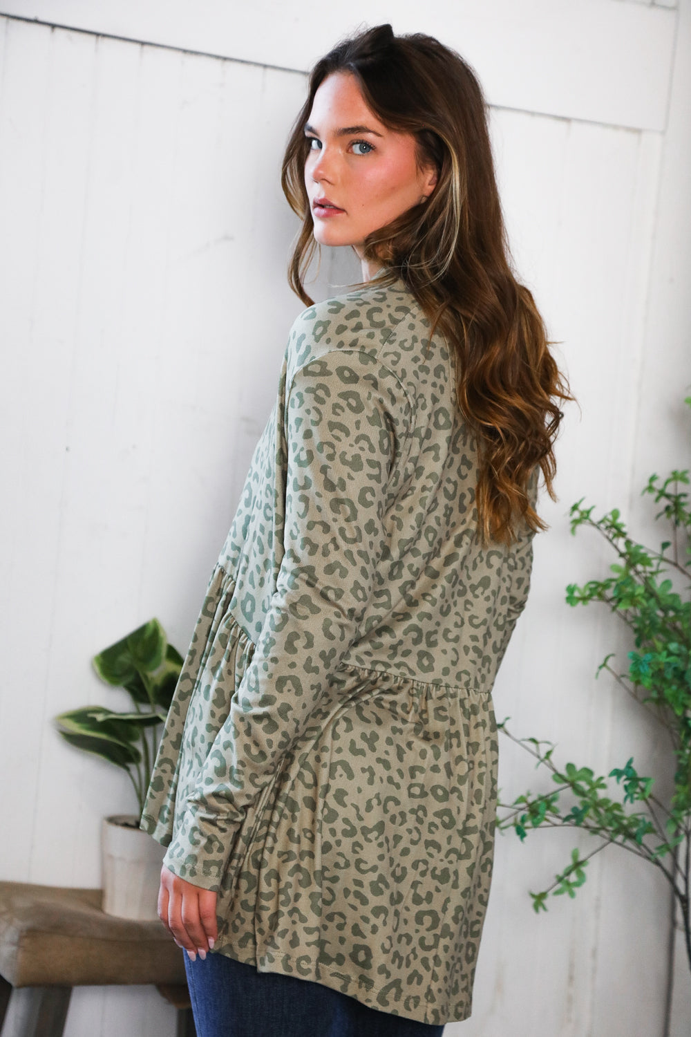 Woman wearing green leopard print peplum cardigan in eclectic, size inclusive setting with plants and casual seating nearby