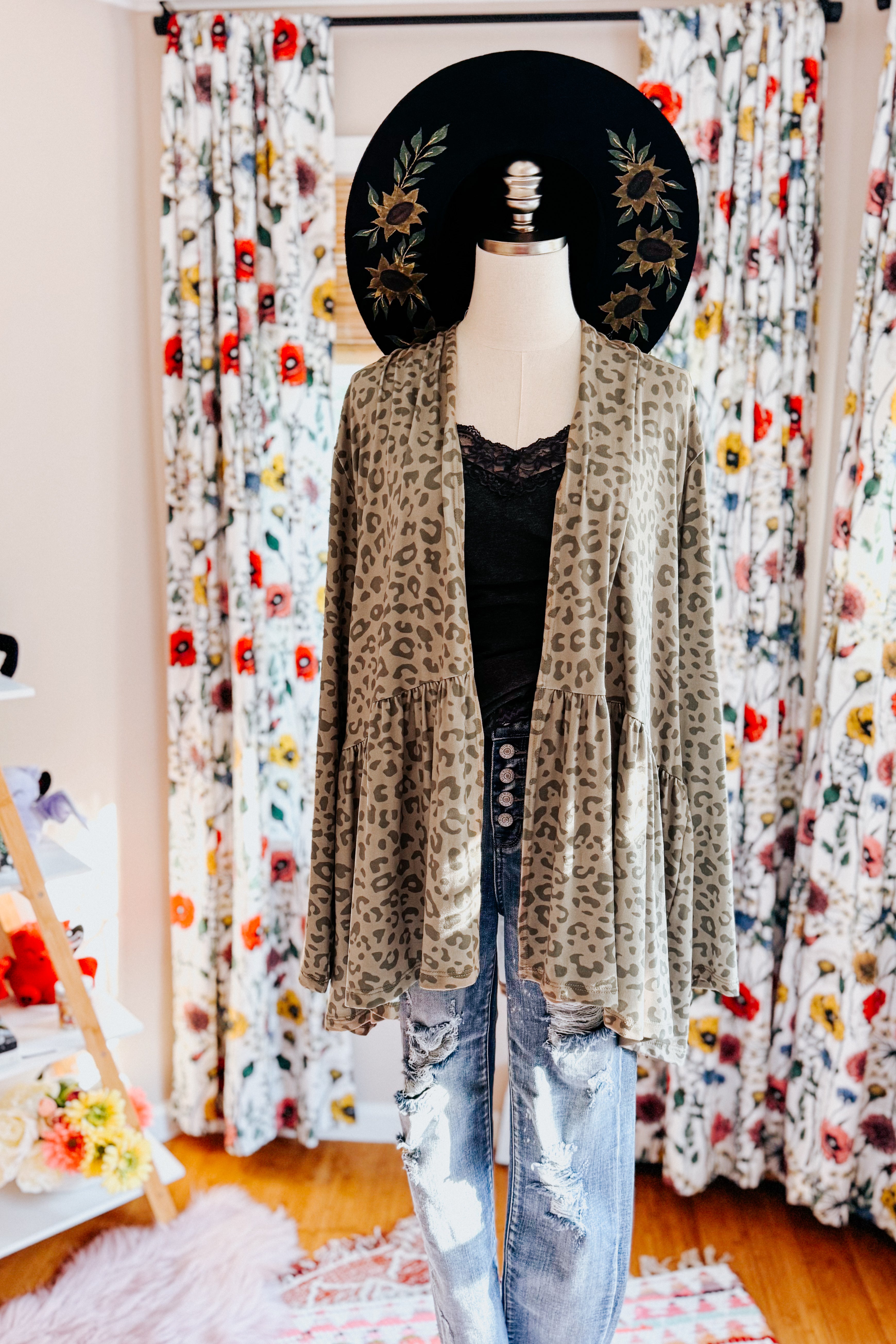 Mannequin dressed in green leopard print peplum cardigan over black lace top and distressed jeans in eclectic room with floral curtains and decor