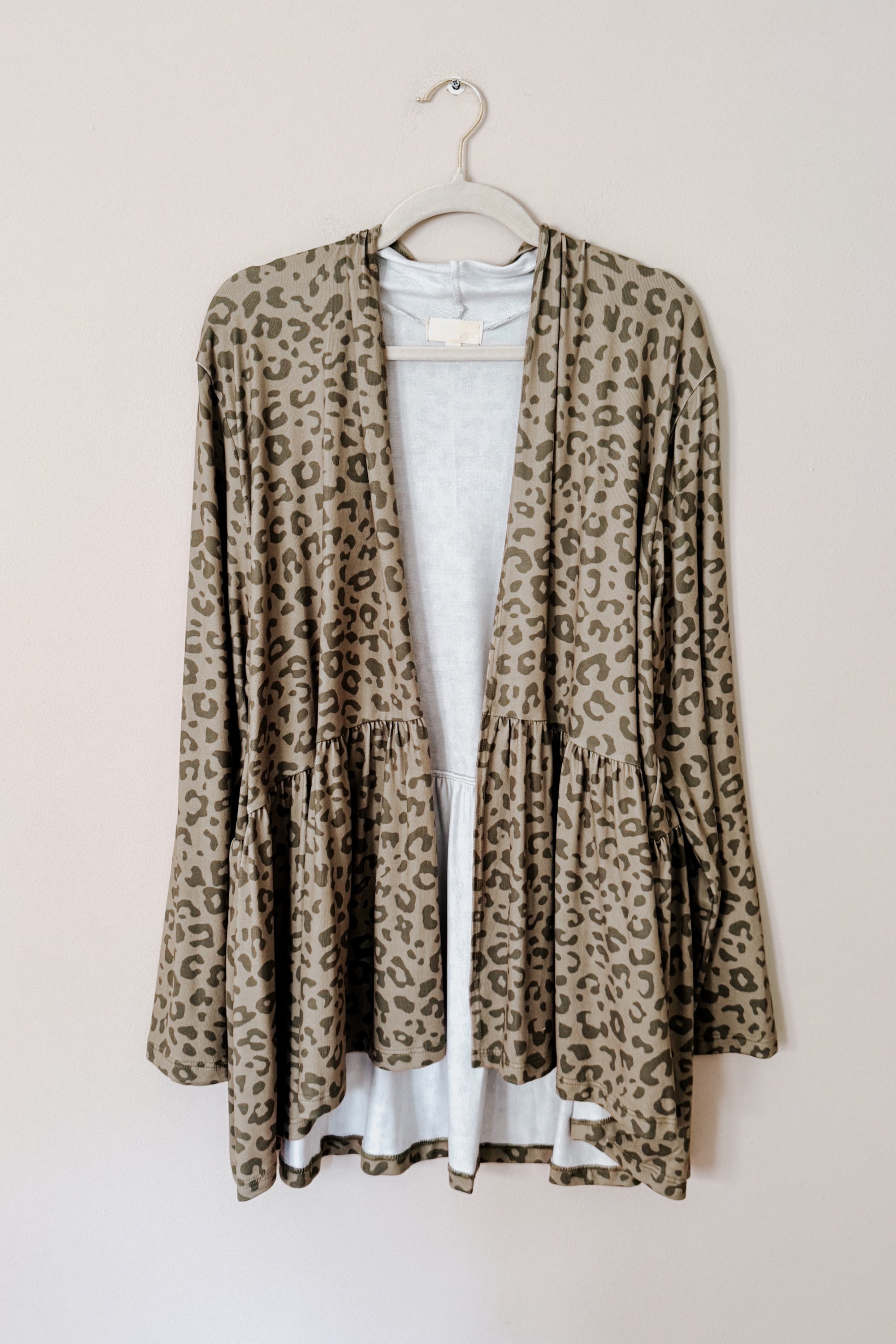 Green leopard print peplum open cardigan with soft drape and relaxed fit hanging against neutral wall