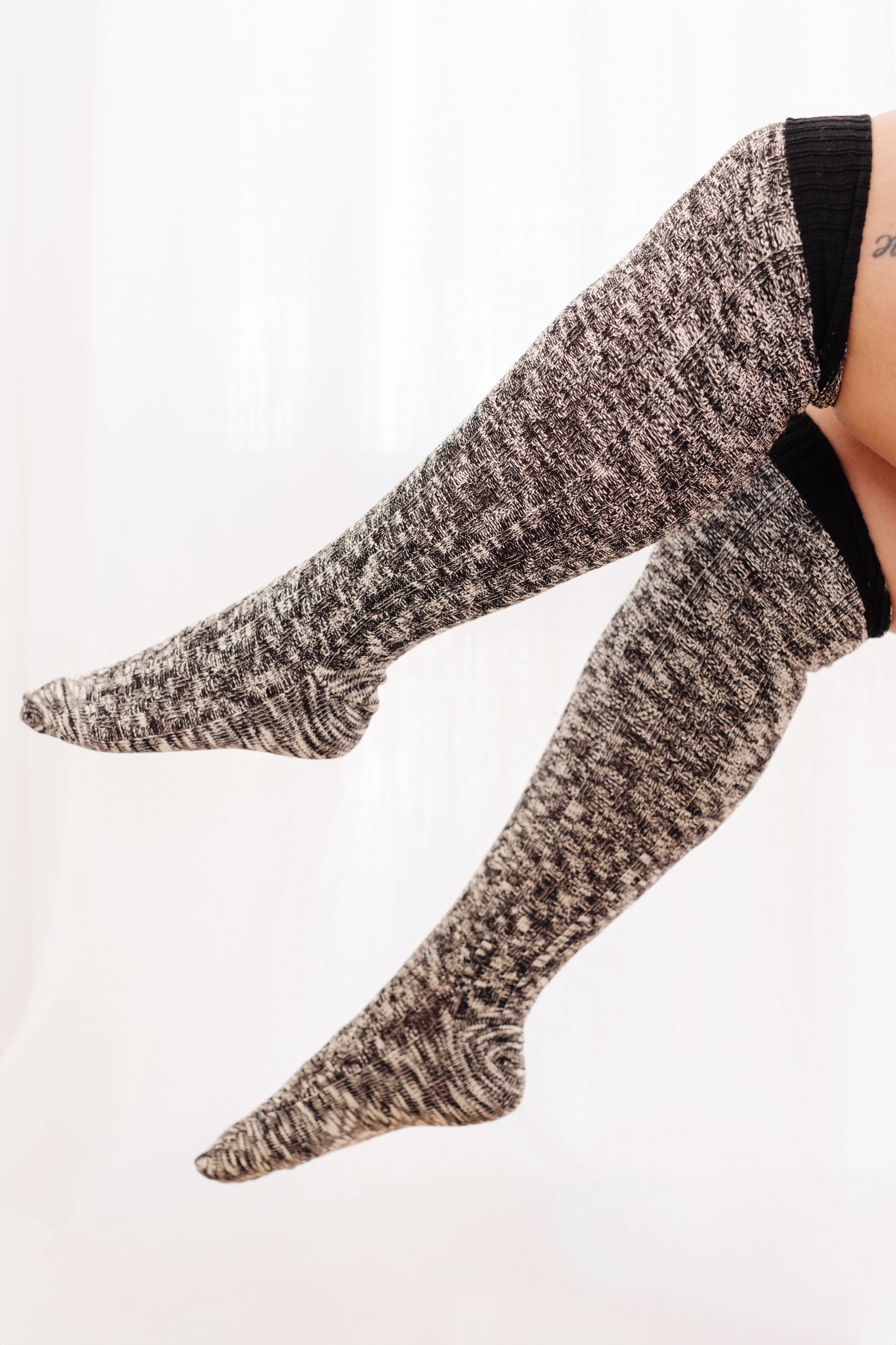 Soft knit lounge socks in cozy black and white marled pattern pulled up to thighs on seated person