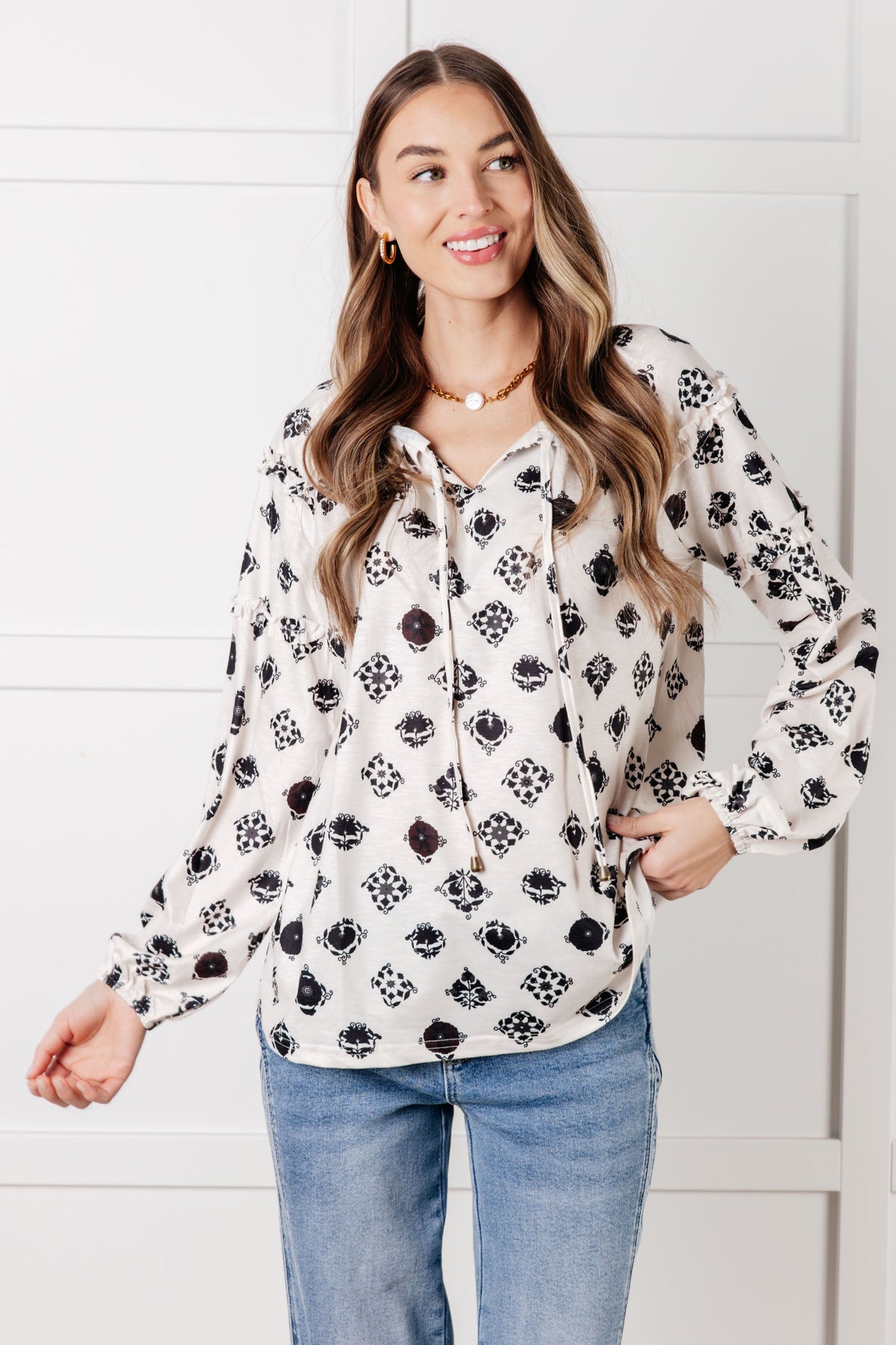 Smiling woman wearing a white floral tile blouse with a split neckline and balloon sleeves styled with blue jeans