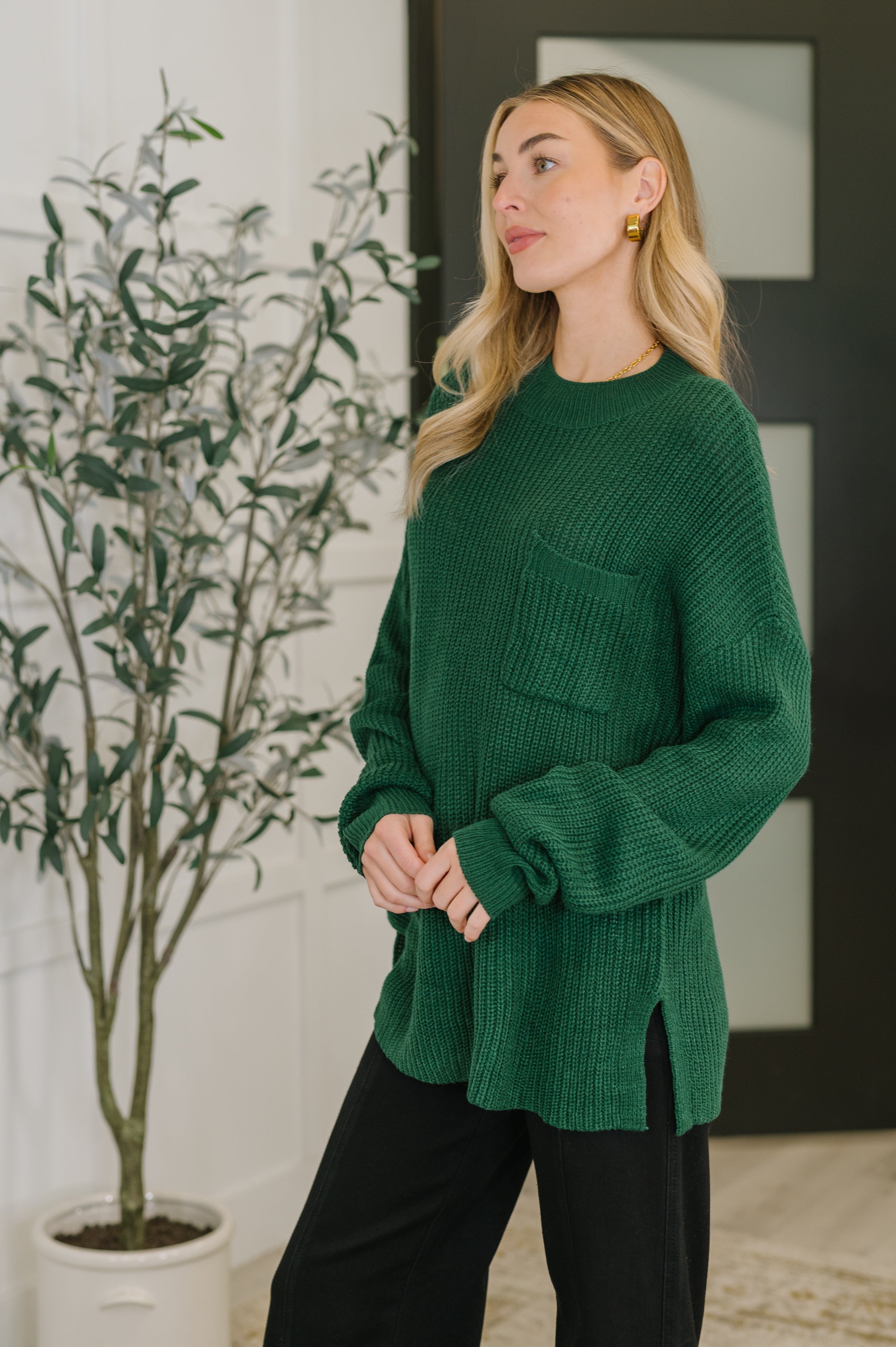 Woman modeling a plush green textured pullover with a front pocket in a softly lit modern room
