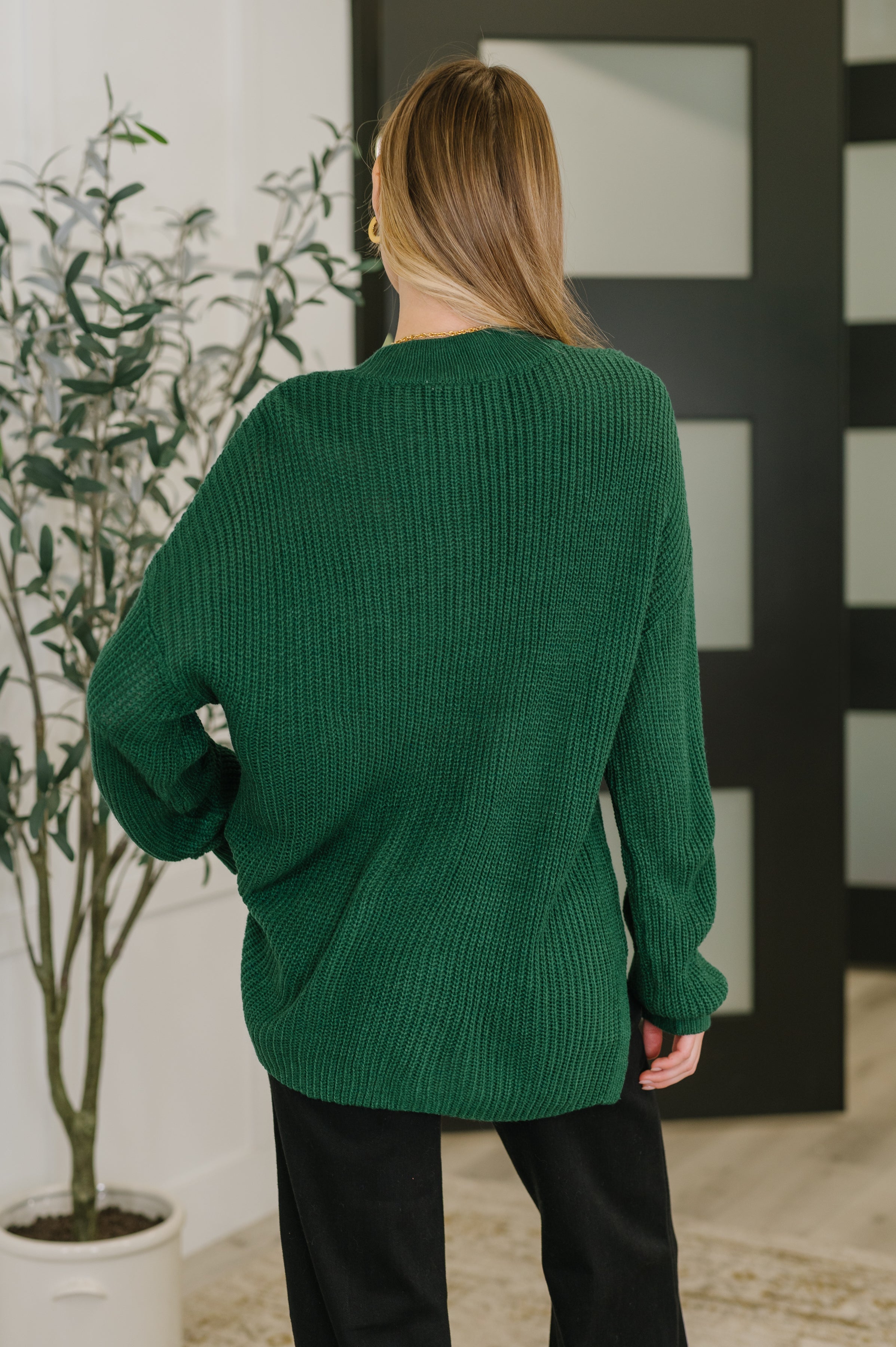 Woman seen from behind wearing a plush green textured pullover with relaxed fit in a modern interior setting