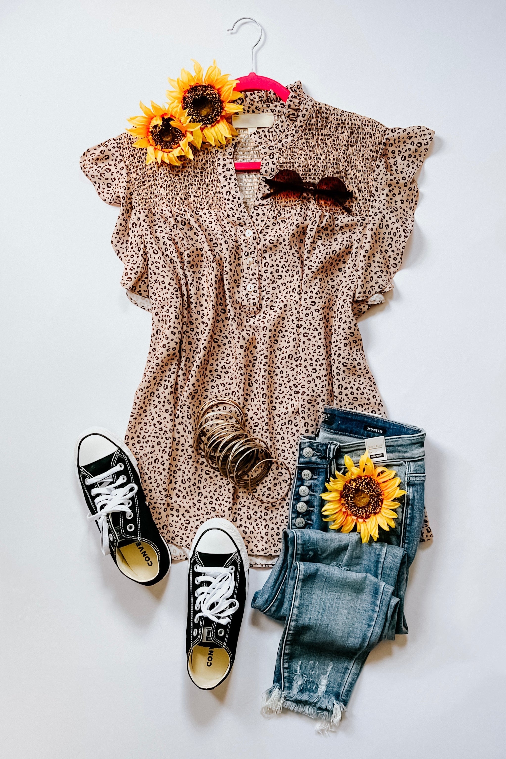 Taupe animal print top with flutter sleeves displayed with black sneakers, distressed jeans, bracelets, and sunflowers