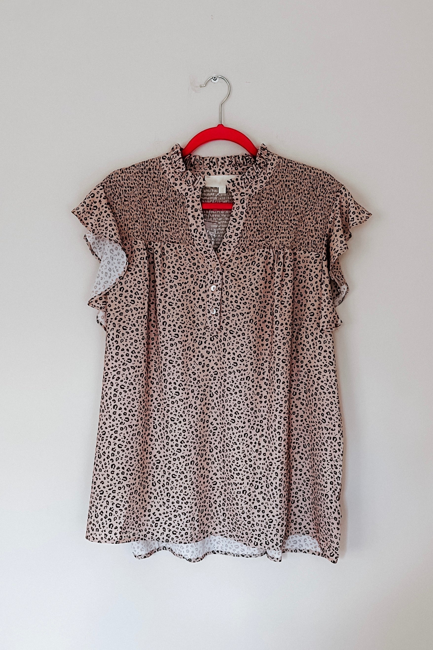 Taupe animal print blouse with flutter sleeves and ruffled collar hanging on red hanger against plain wall