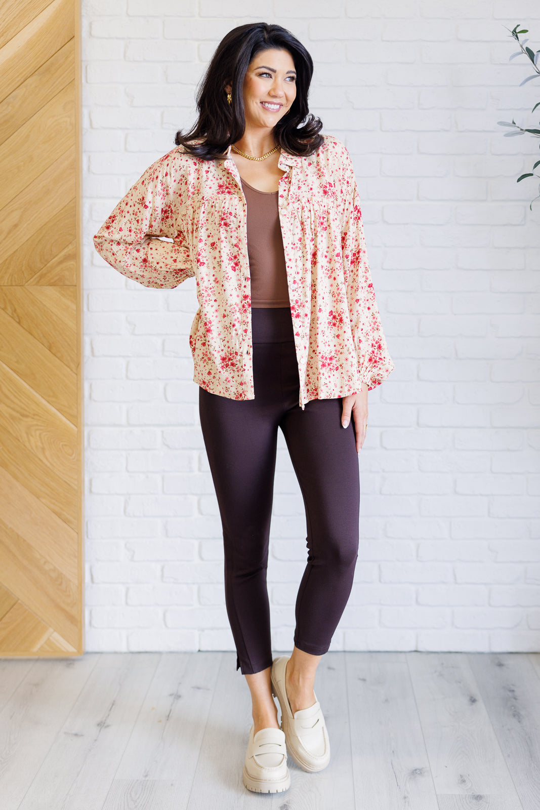 Smiling woman styling a pink floral collared button down with balloon sleeves over a brown top and fitted leggings with white platform loafers indoors