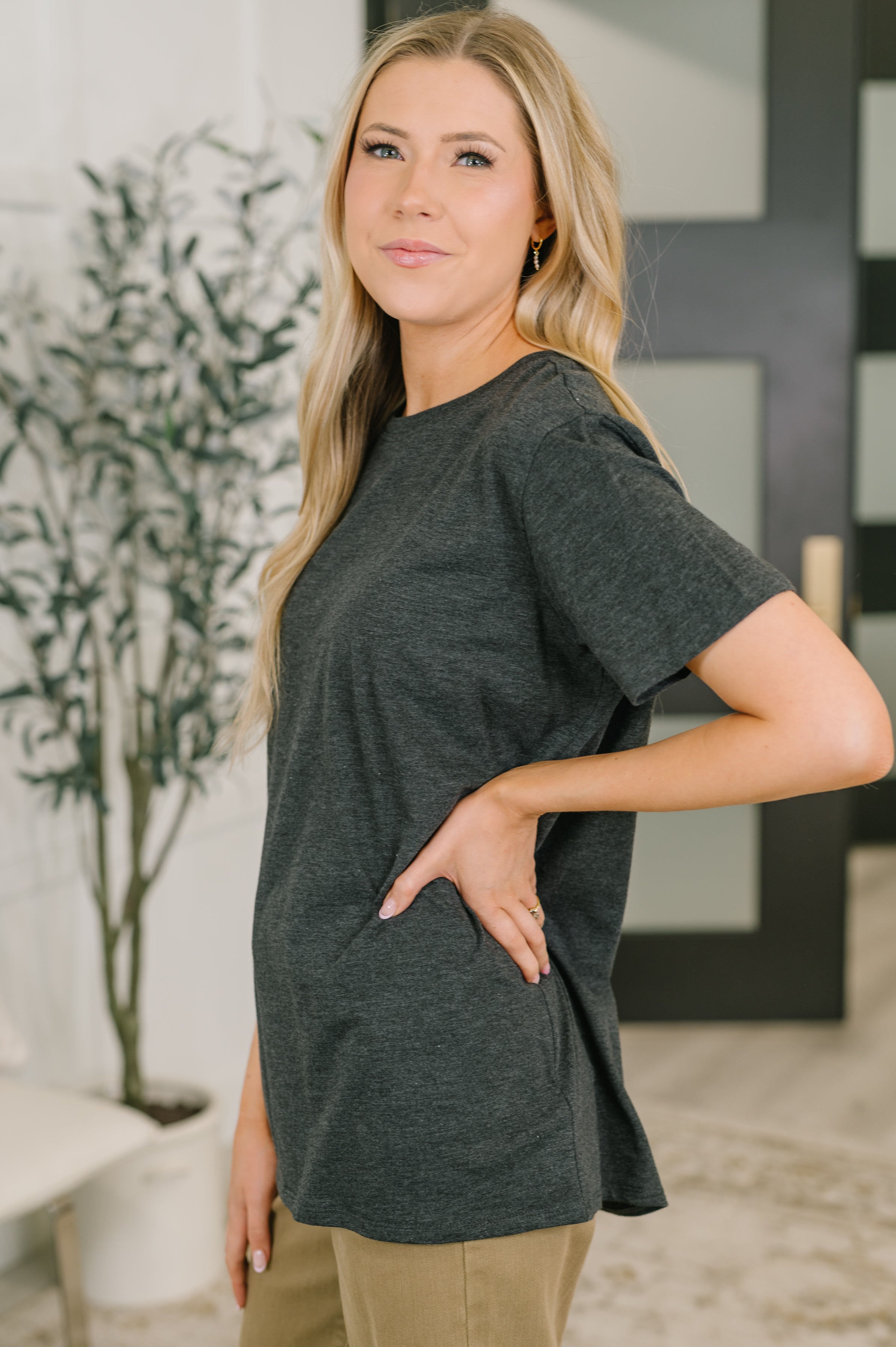 Woman wearing charcoal relaxed-fit soft jersey tee paired with tan pants in a modern indoor space