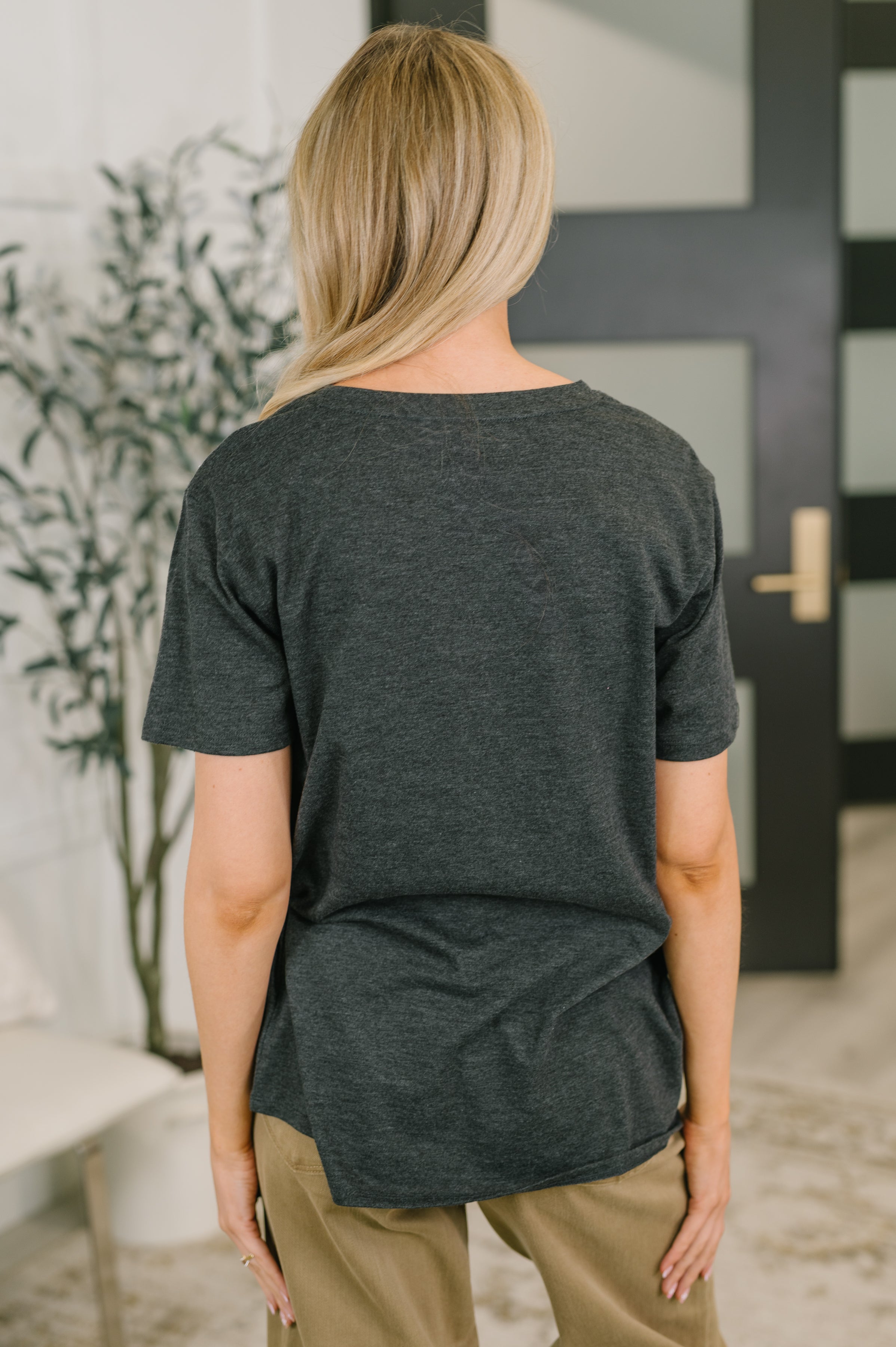 Woman wearing relaxed charcoal jersey knit tee with short sleeves paired with beige pants in modern indoor space