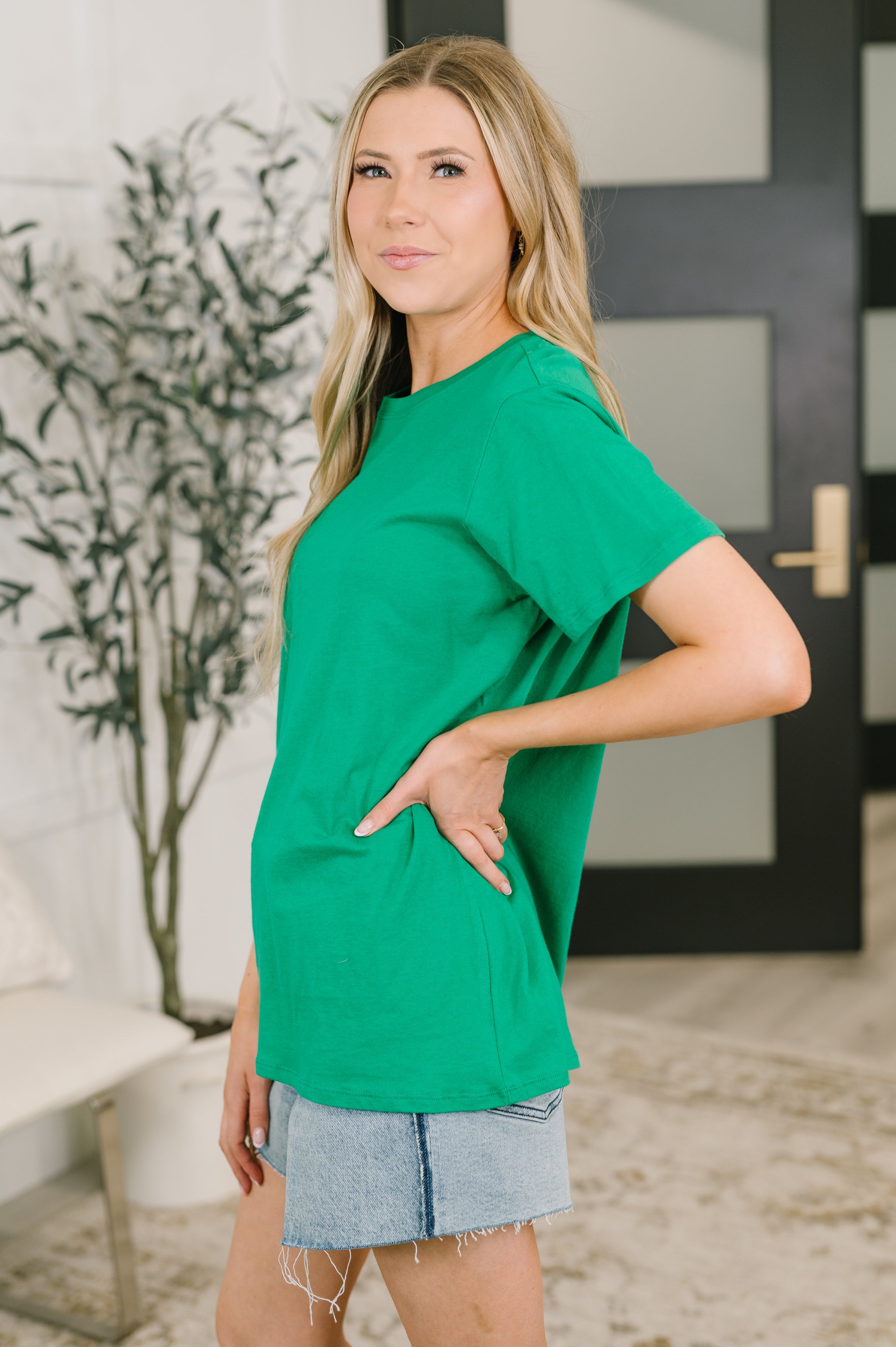 Woman wearing vibrant green relaxed fit tee with short sleeves paired with light denim skirt in casual indoor setting