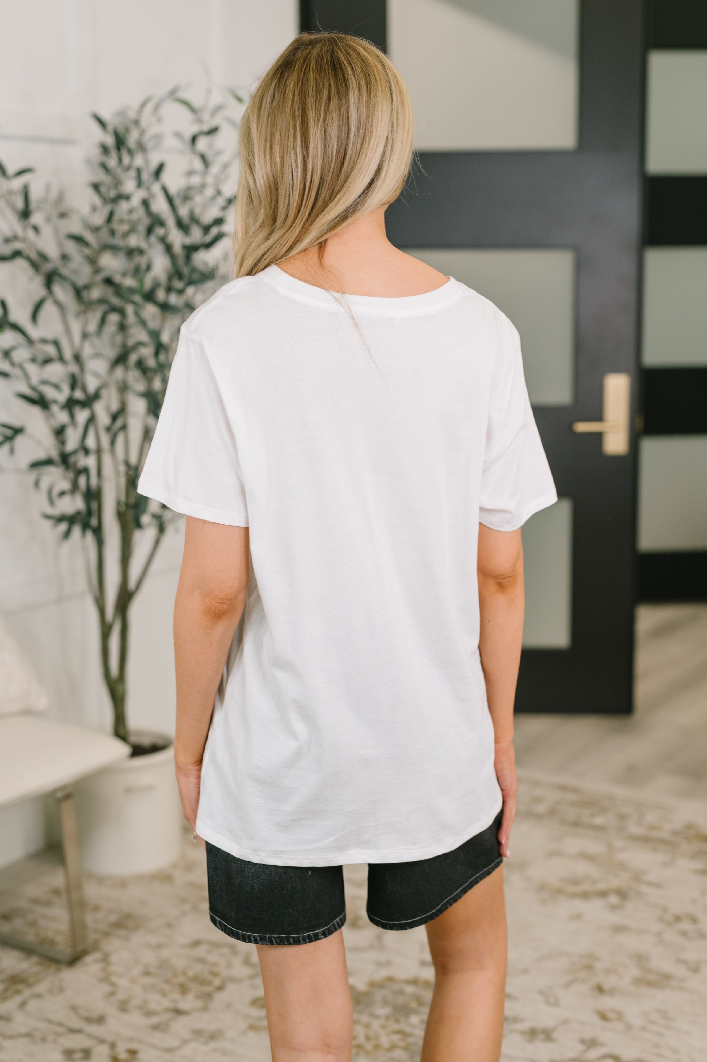 Back view of woman wearing white relaxed fit tee paired with black denim shorts in bright indoor space